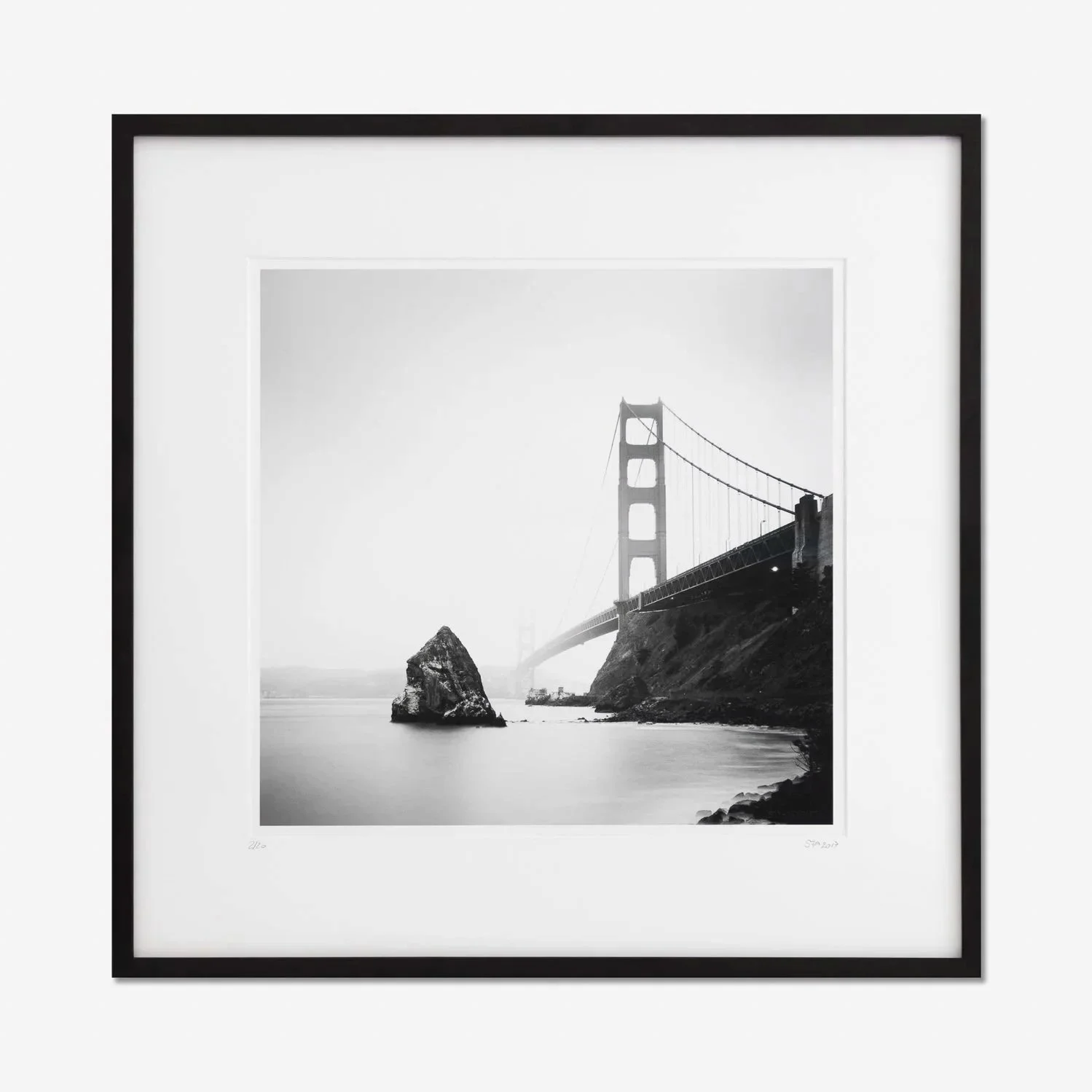 Black-framed black-and-white fine art photograph of the Golden Gate Bridge, San Francisco, with a solitary coastal rock and calm water, by Gerald Berghammer.