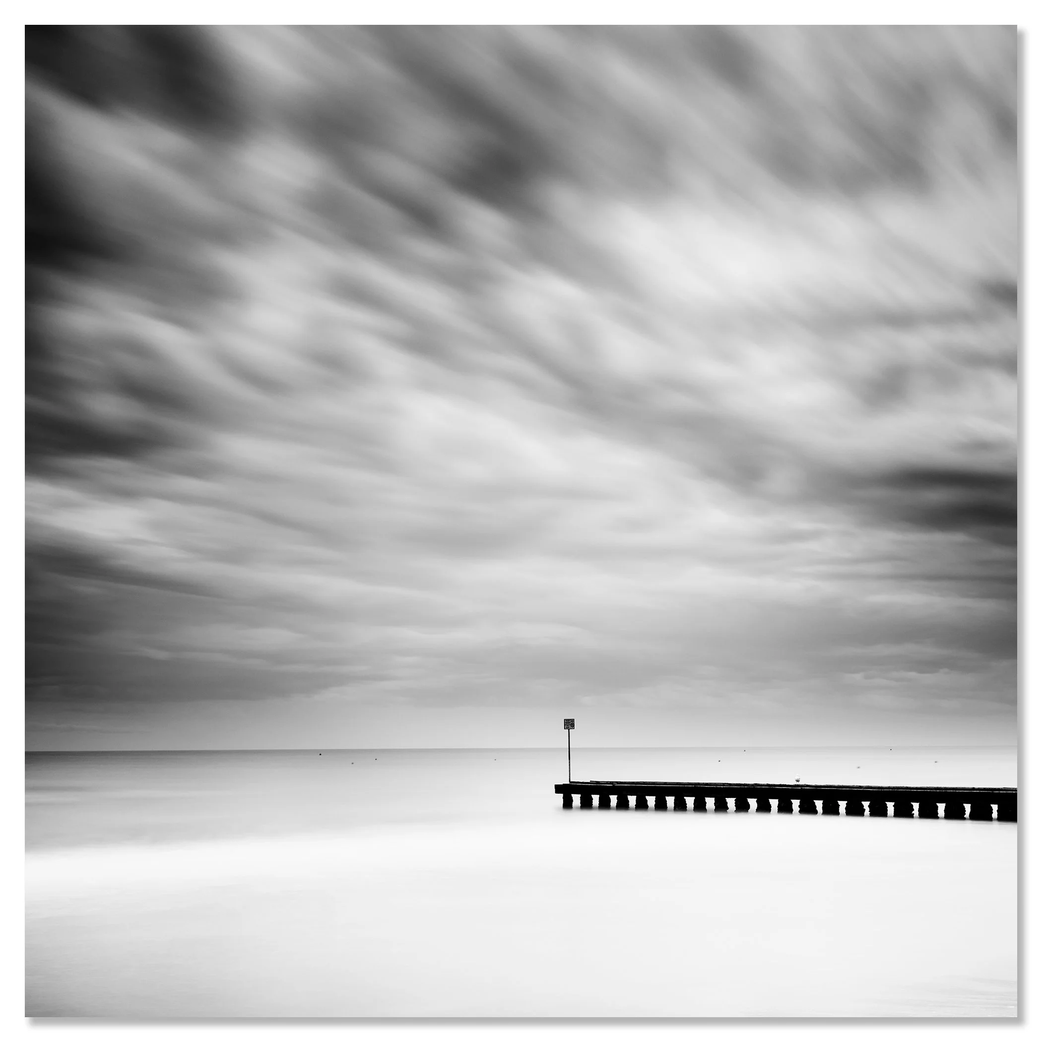 Fine art black and white seascape with moving clouds and a pier reaching towards the horizon – dibond frameless