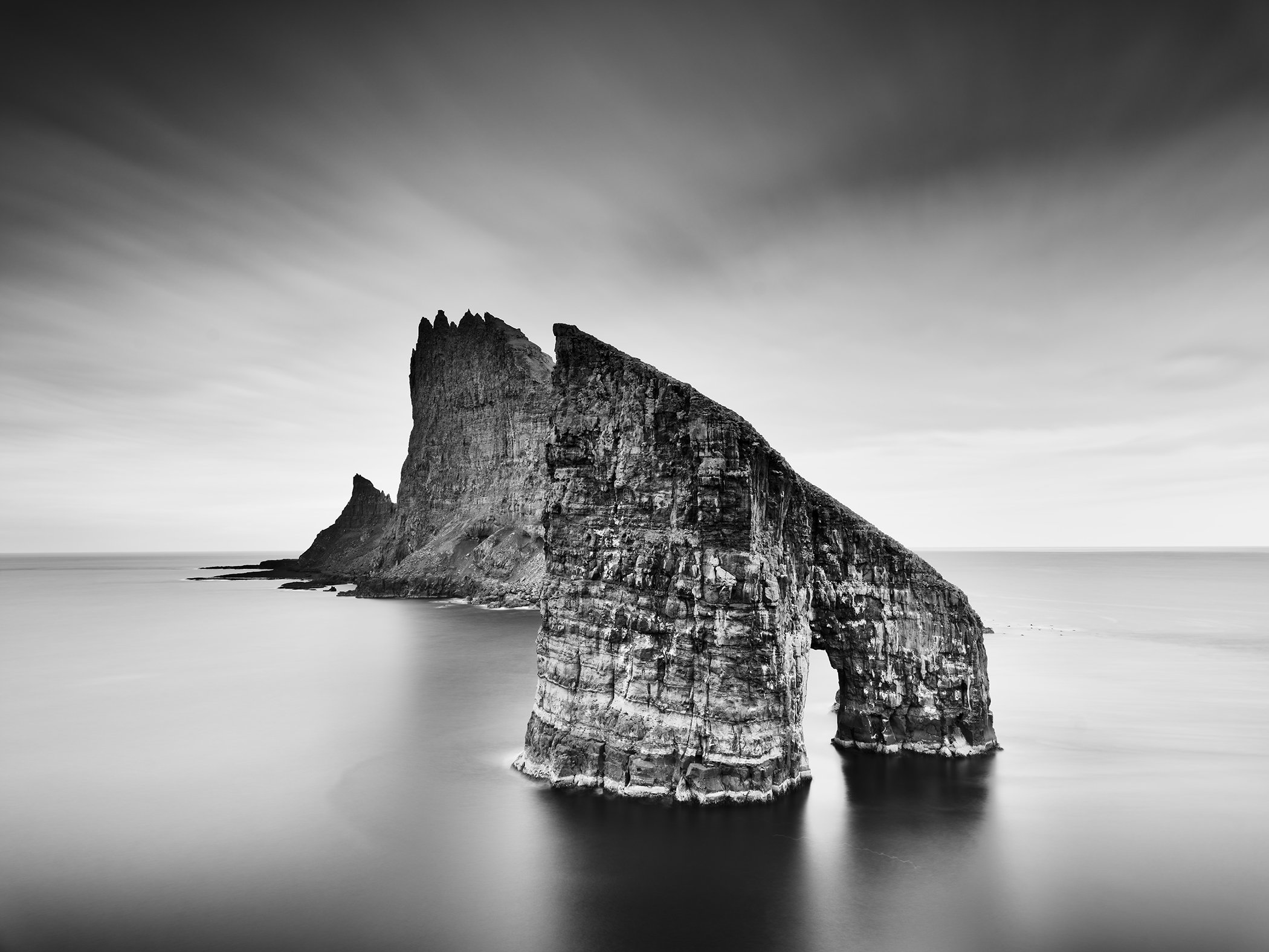 Fine art black and white photo of towering coastal cliffs and calm sea in the Faroe Islands by Gerald Berghammer.