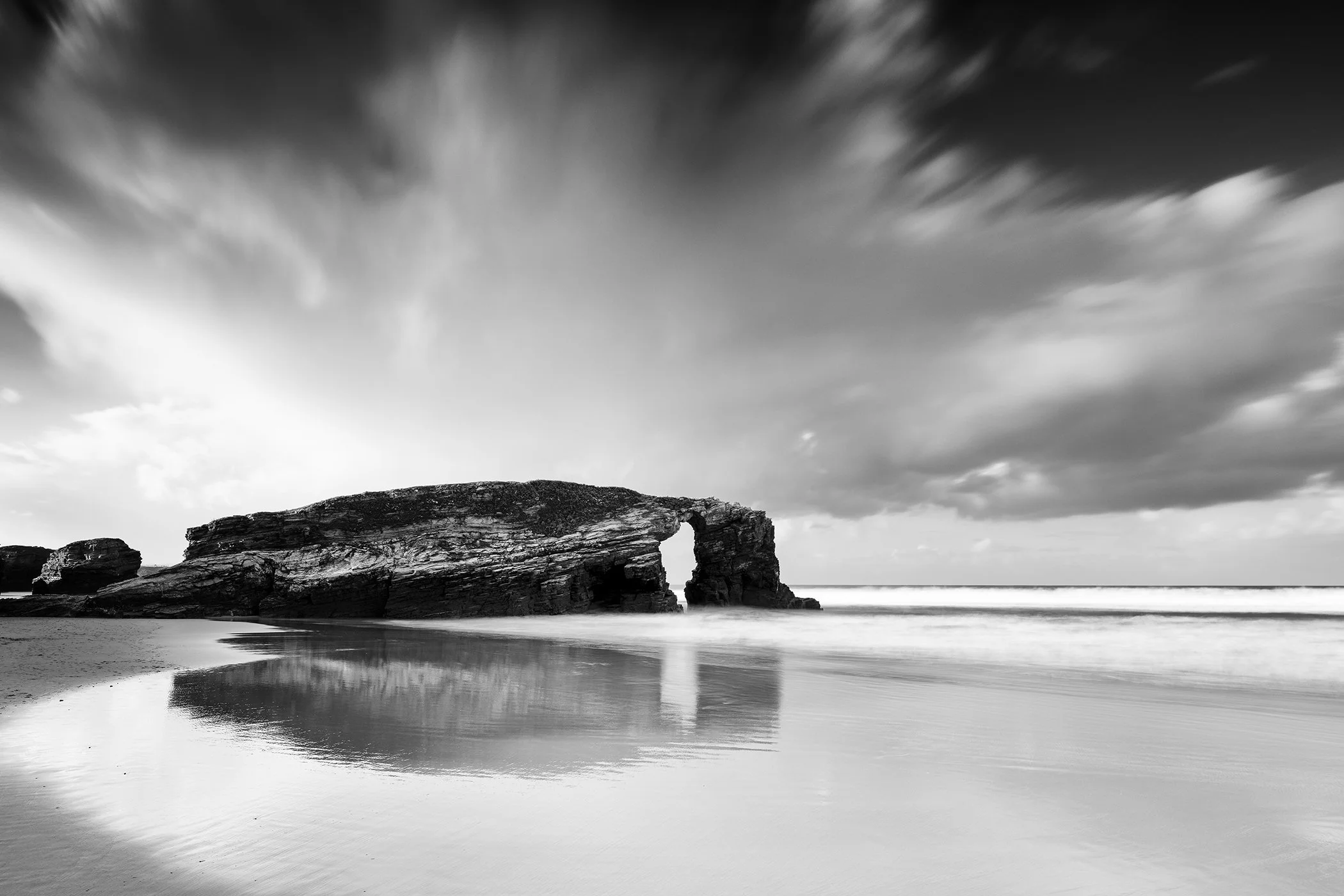 Rock arch and shoreline at As Catedrais Beach, Spain in a black-and-white long-exposure seascape photograph.