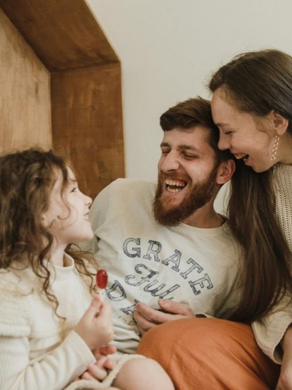A mom and dad are laughing with their daughter.