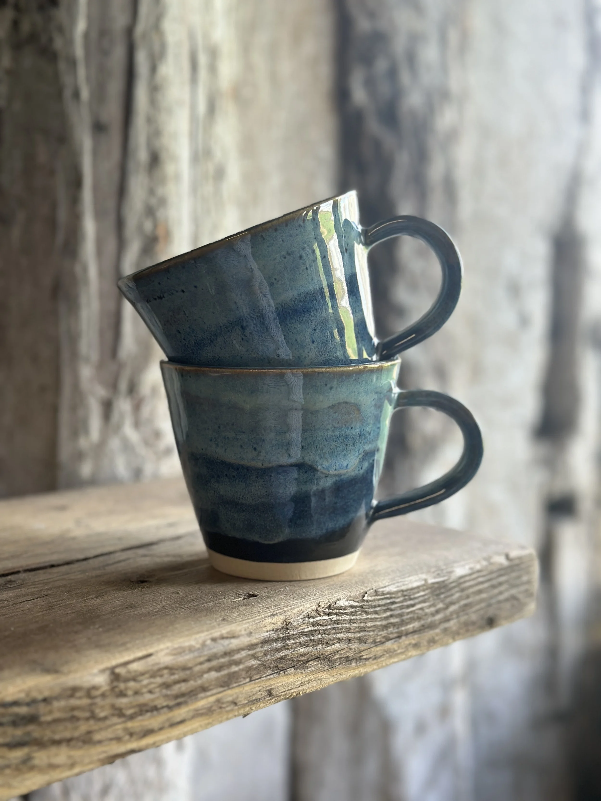 Two coffee mugs or tea cups made from white stoneware clay and glazed in a flowing blue glaze inspired by the sea