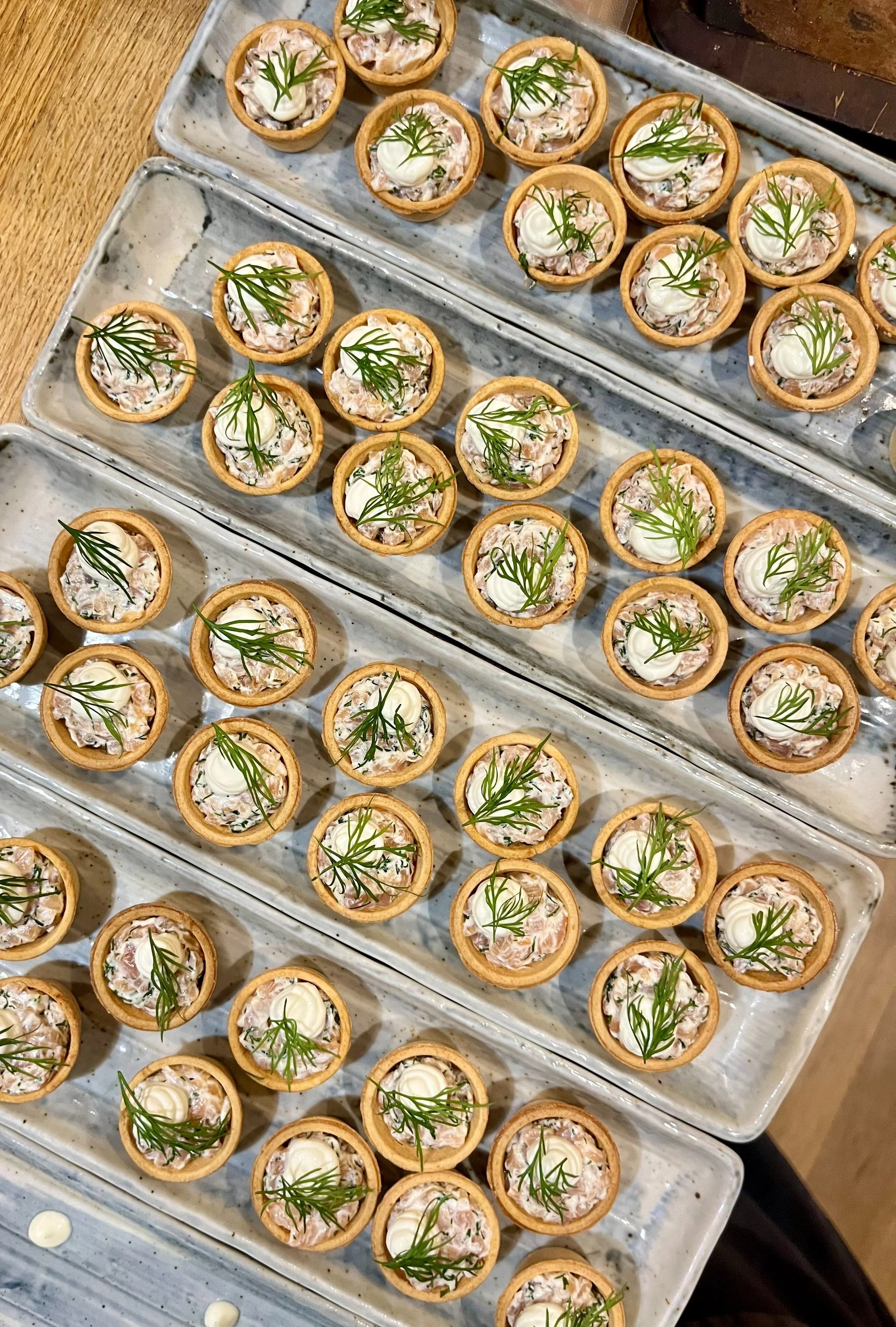 Mini tartlets with creamy filling, garnished with fresh herbs, arranged on gray ceramic trays.