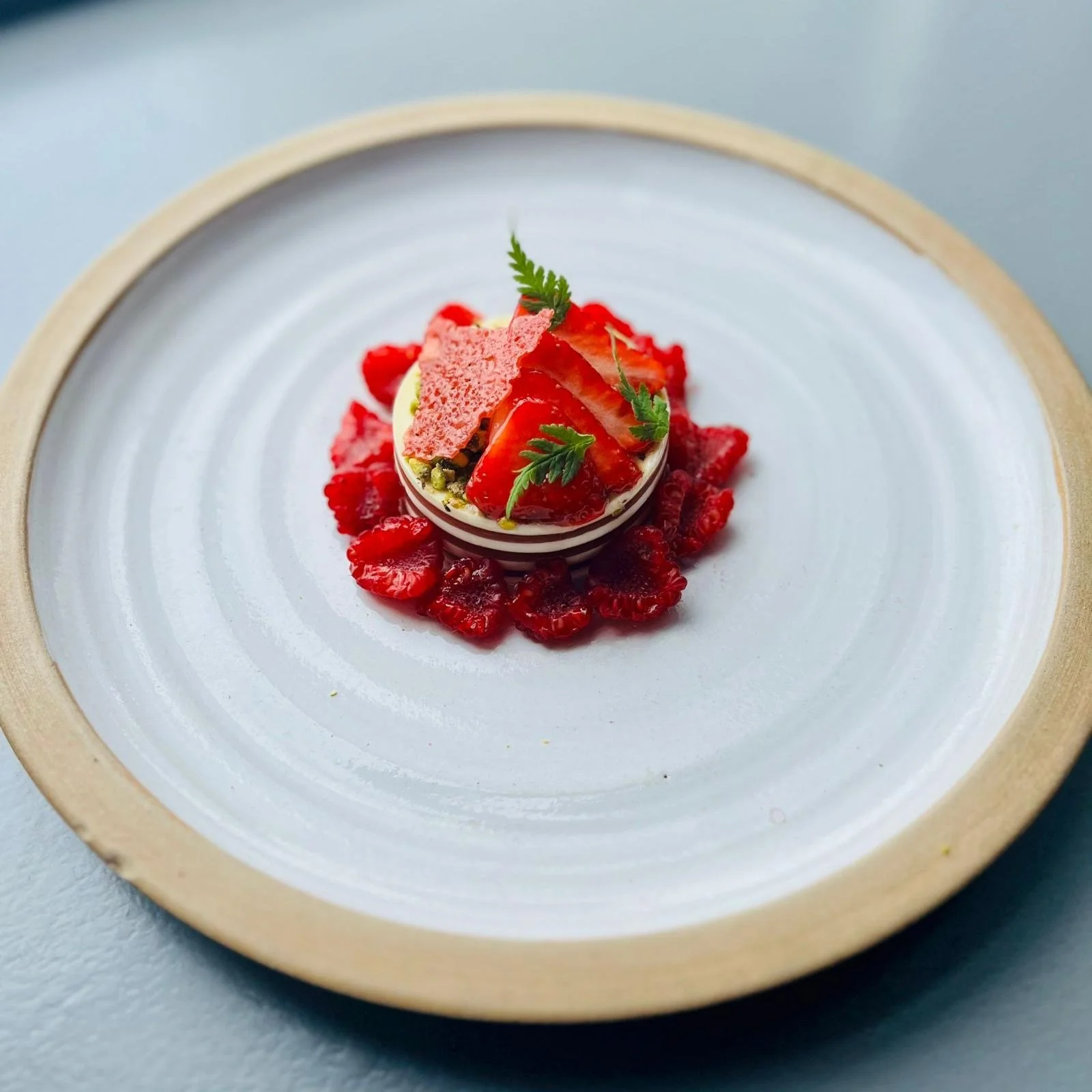 A dessert with fresh strawberries, garnished with small green leaves, served on a white ceramic plate with a light wooden rim.