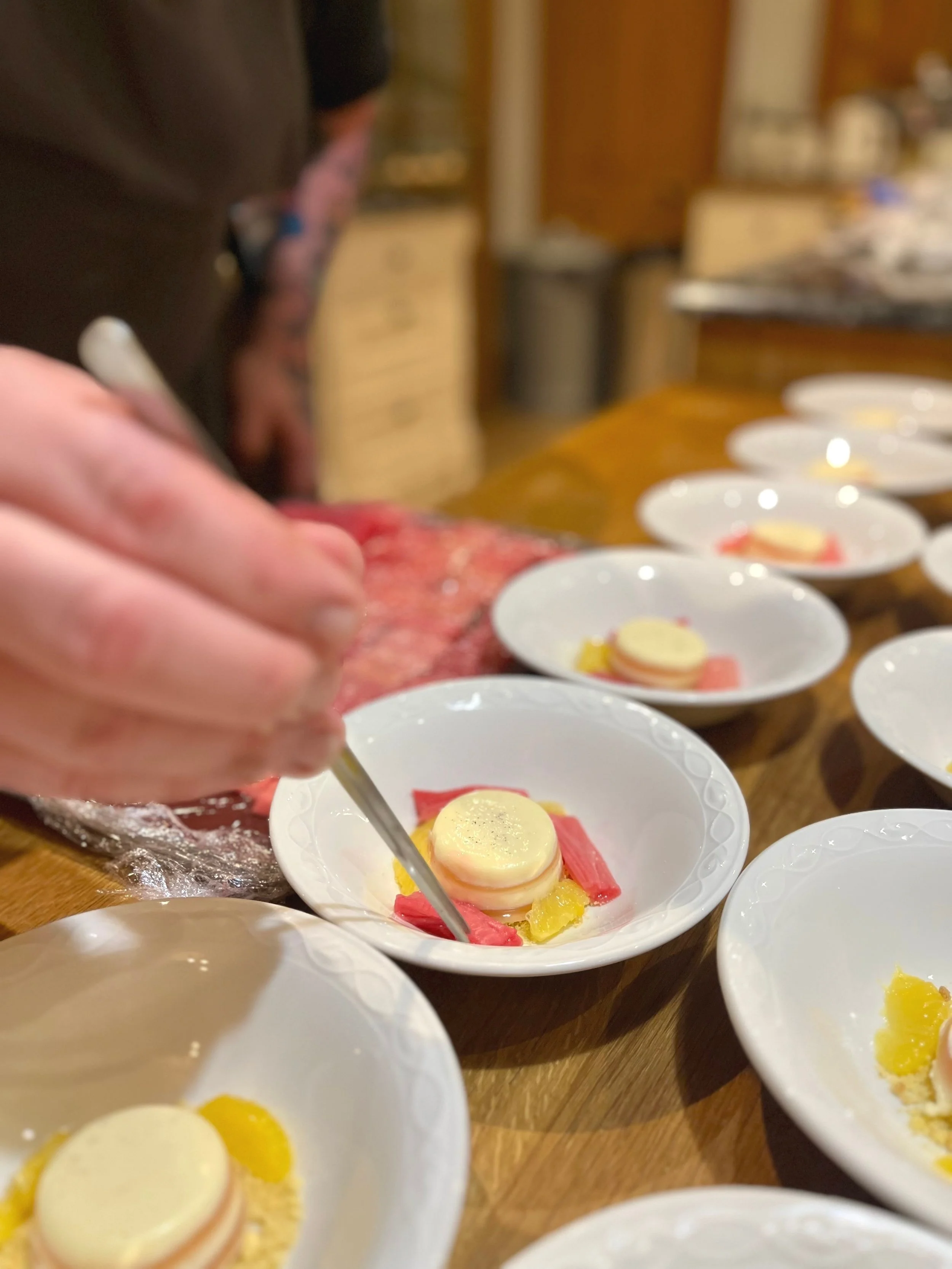 A chef preparing layered appetizer dishes with yellow, pink, and white ingredients on a wooden counter.