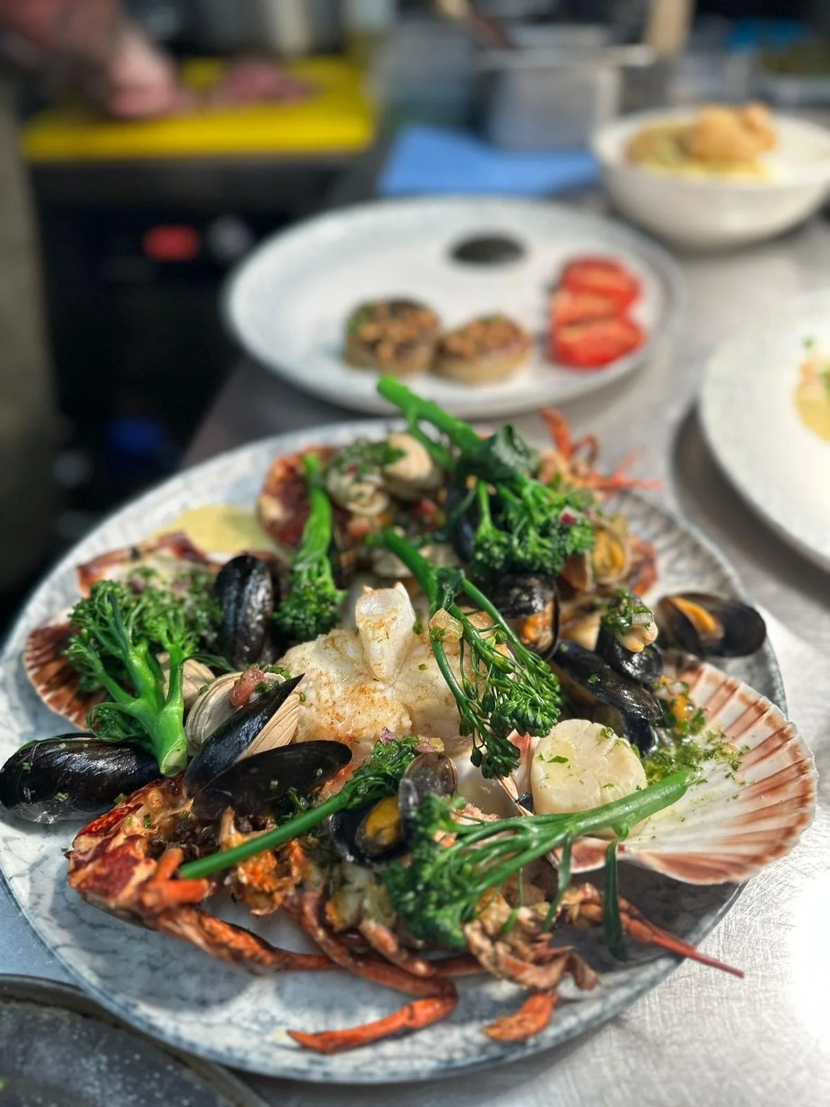 Seafood dish with lobster, mussels, broccolini, and vegetables on a white plate.