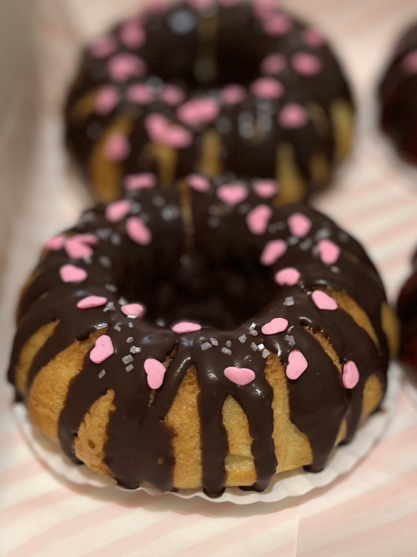 close up front view of vanilla bundt cakes with chocolate ganache and pink heart sprinkles