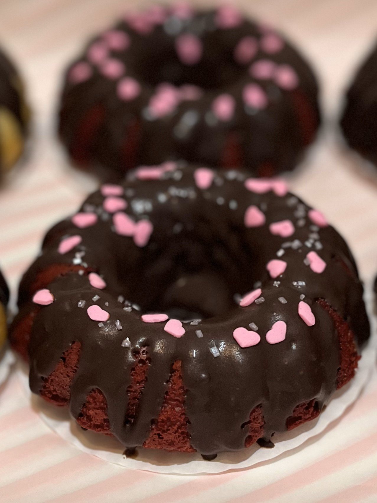 close up front view of red velvet bundt cakes with chocolate ganache and pink heart sprinkles