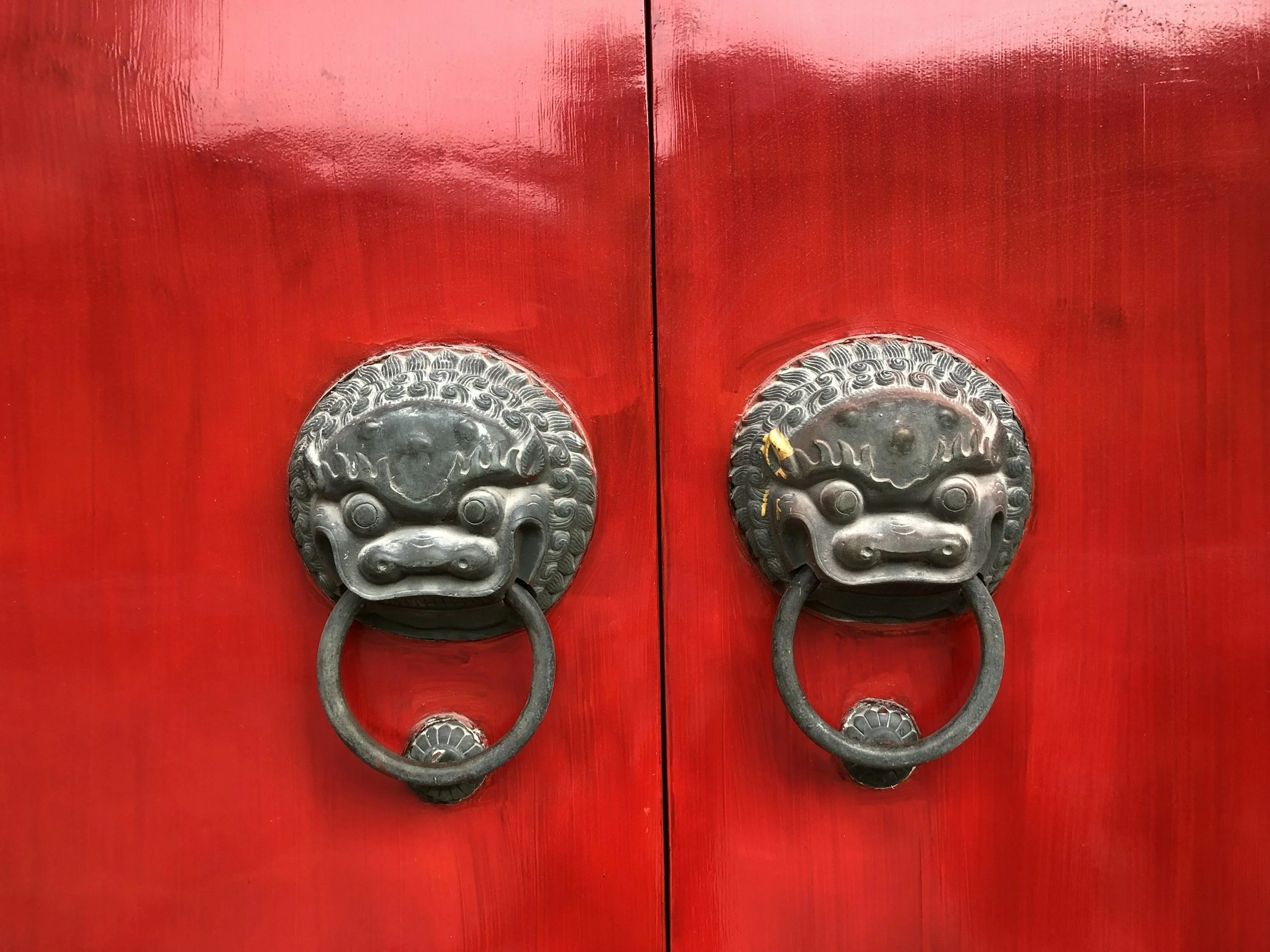 Deux poignées de porte avec des têtes de lion en métal sur un fond rouge