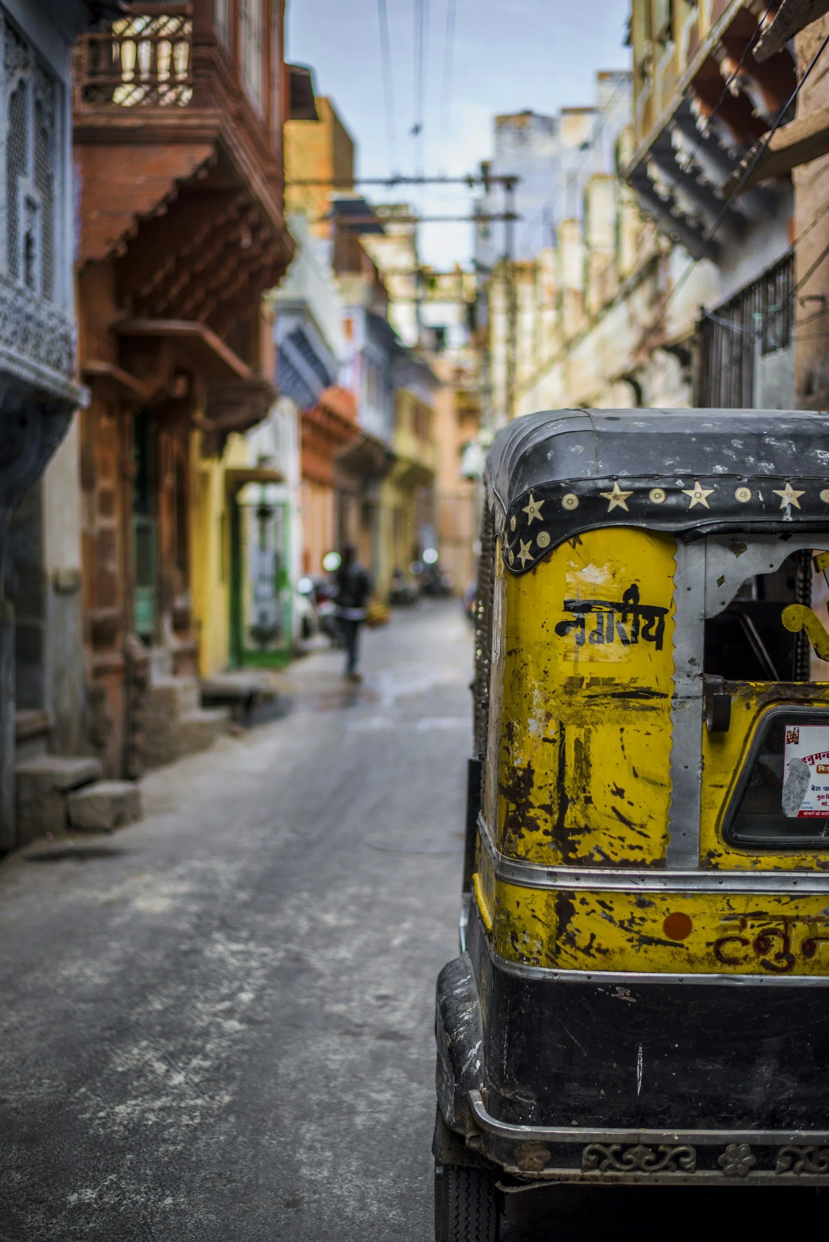Une ruelle étroite avec des bâtiments colorés et une auto- rickshaw jaune au premier plan.