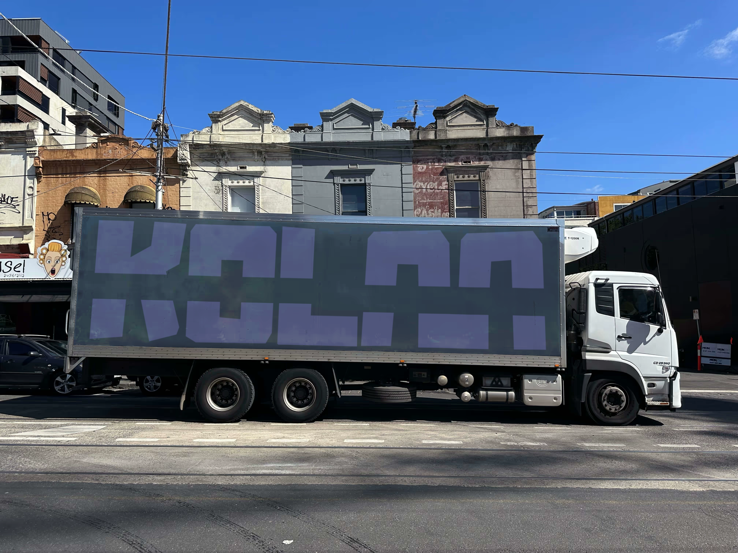 Un camion de livraison blanc avec une grande surface latérale en arrière-plan d'un bâtiment urbain, sous un ciel bleu clair.