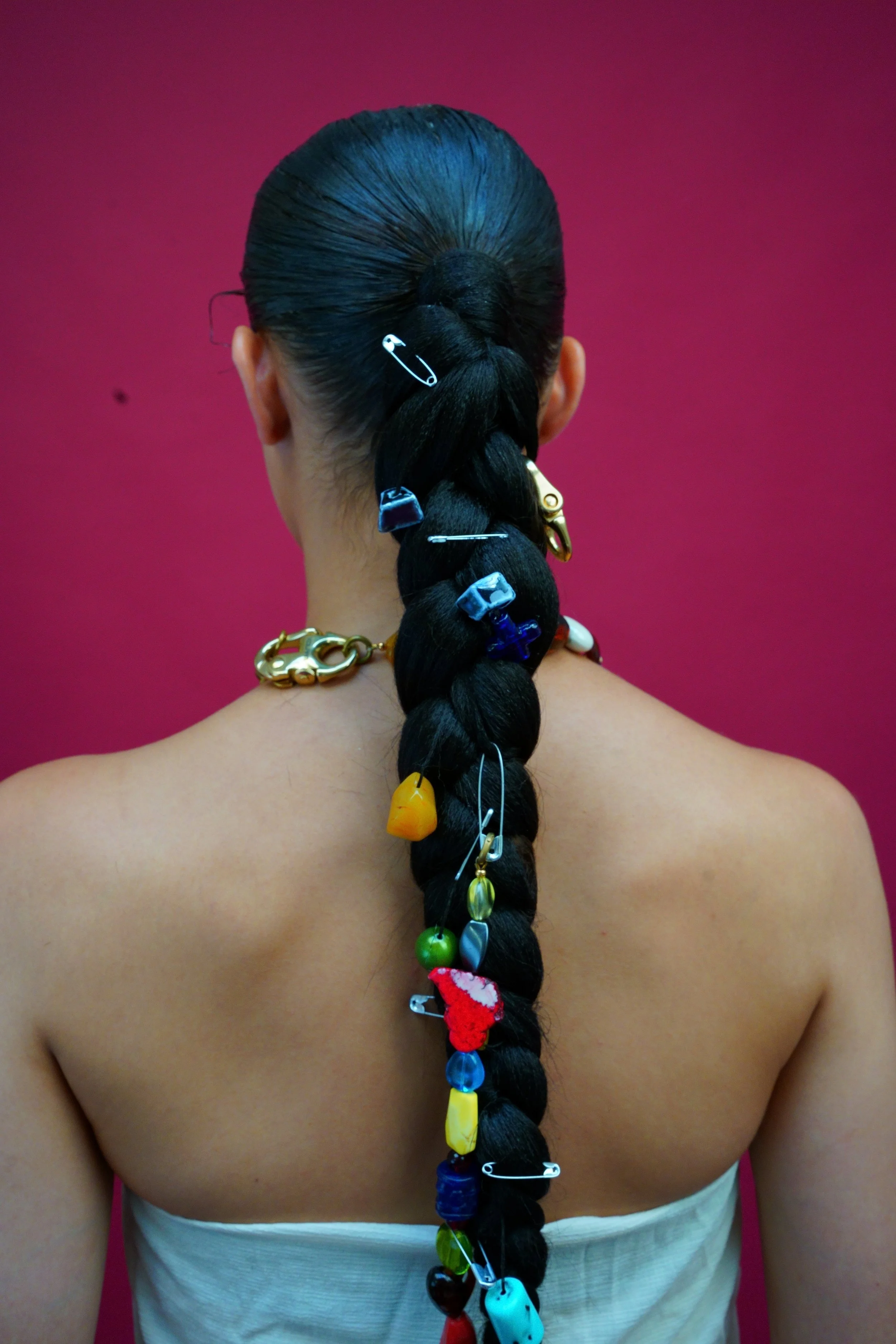 Coiffure longue avec des épingles à cheveux multicolores attachée dans une queue de cheval sur une personne vue de dos, avec un fond rouge.