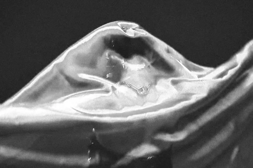 Goutte d'eau sur une surface translucide, avec un fond noir.