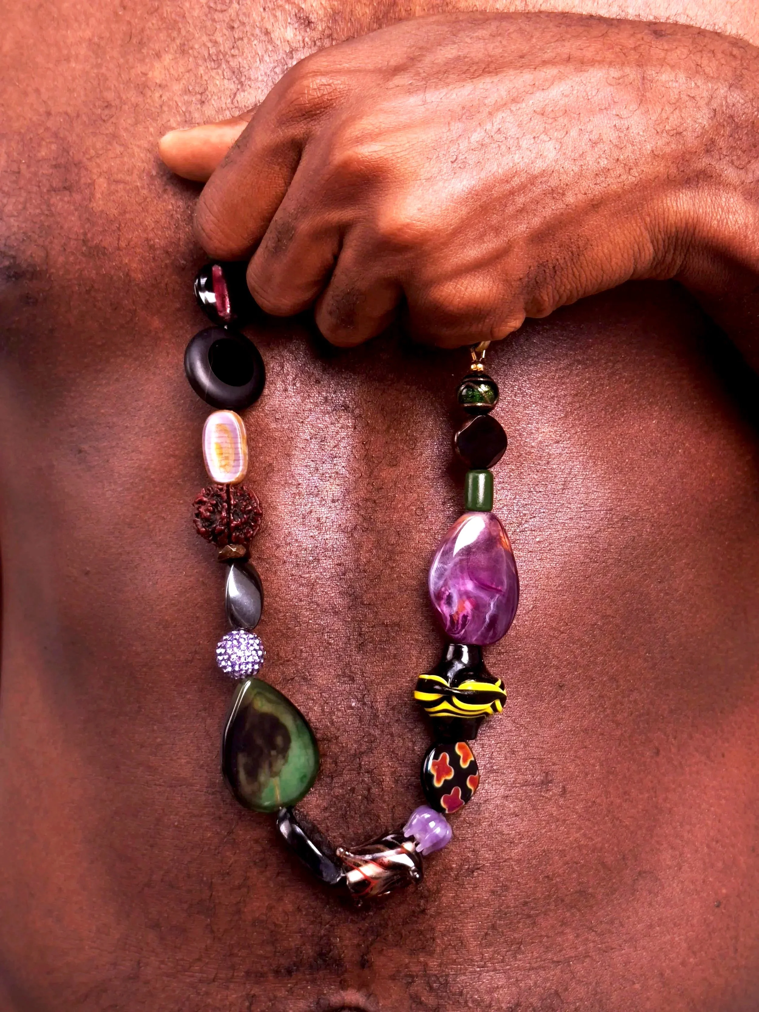Un collier de perles et de pierres de différentes couleurs et formes, suspendu à un torse humain nu.