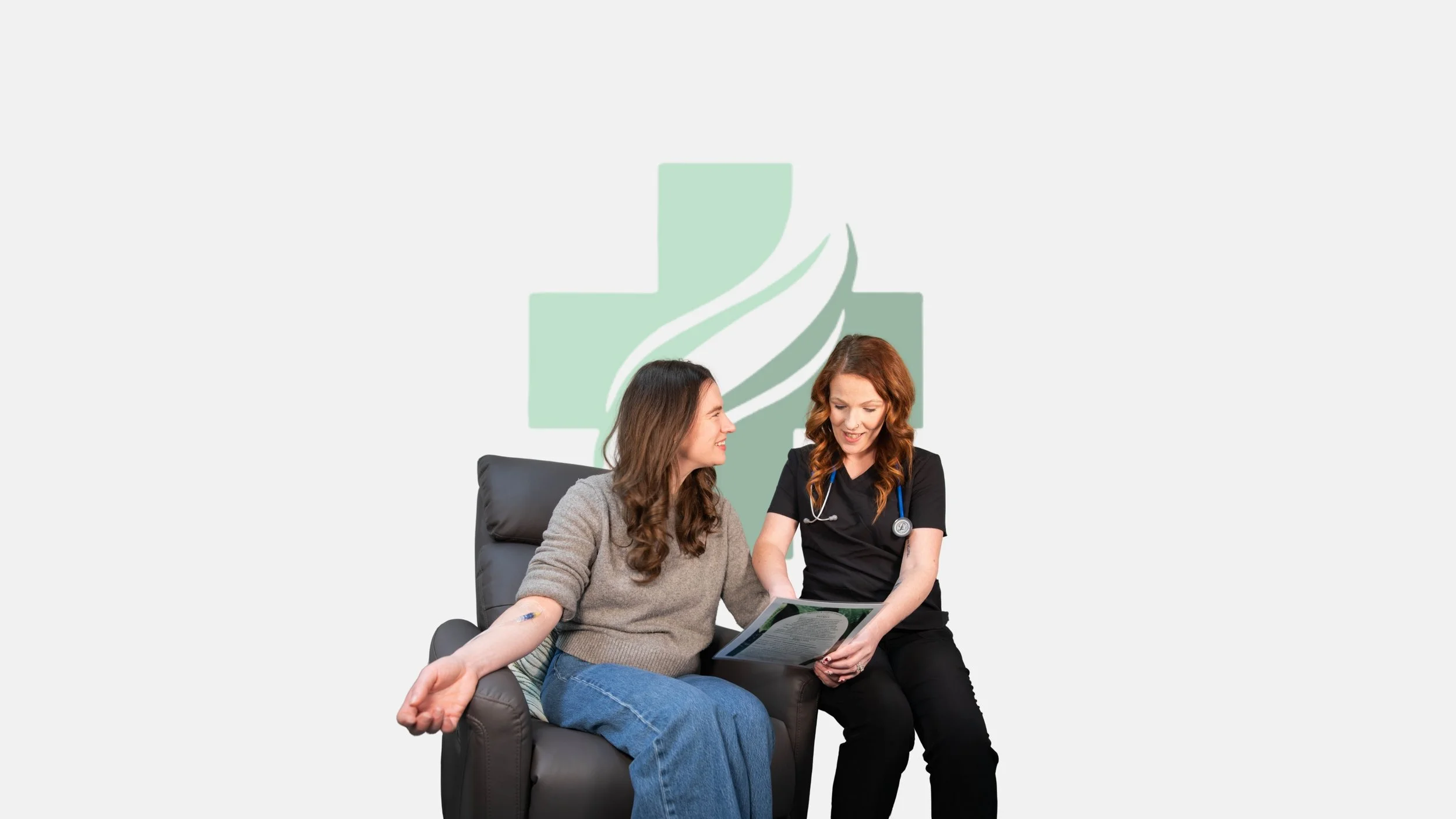 A young woman in a gray sweater and jeans sits on a black chair, smiling at a female healthcare professional in black scrubs with a stethoscope. The healthcare professional shows her a clipboard or medical chart. A medical cross with a leaf and a staff is displayed in the background.