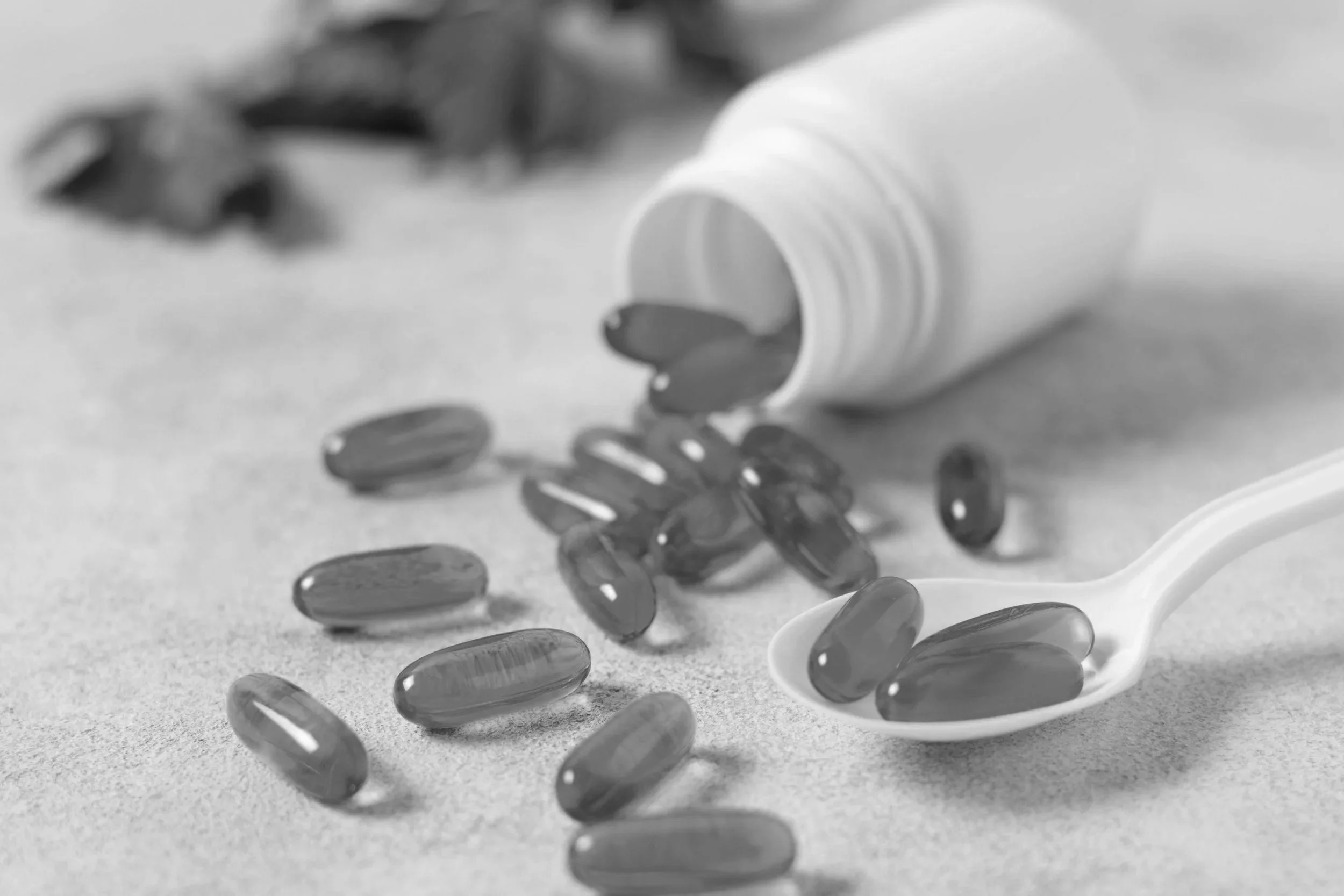 A white pill bottle tipped over with capsules spilling out onto a surface, and a white spoon holding some capsules.