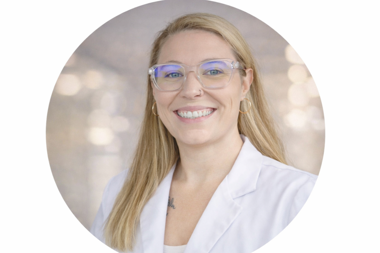 A female healthcare professional with dreadlocks wearing a white lab coat and stethoscope, standing in a bright, modern medical facility or hospital corridor.