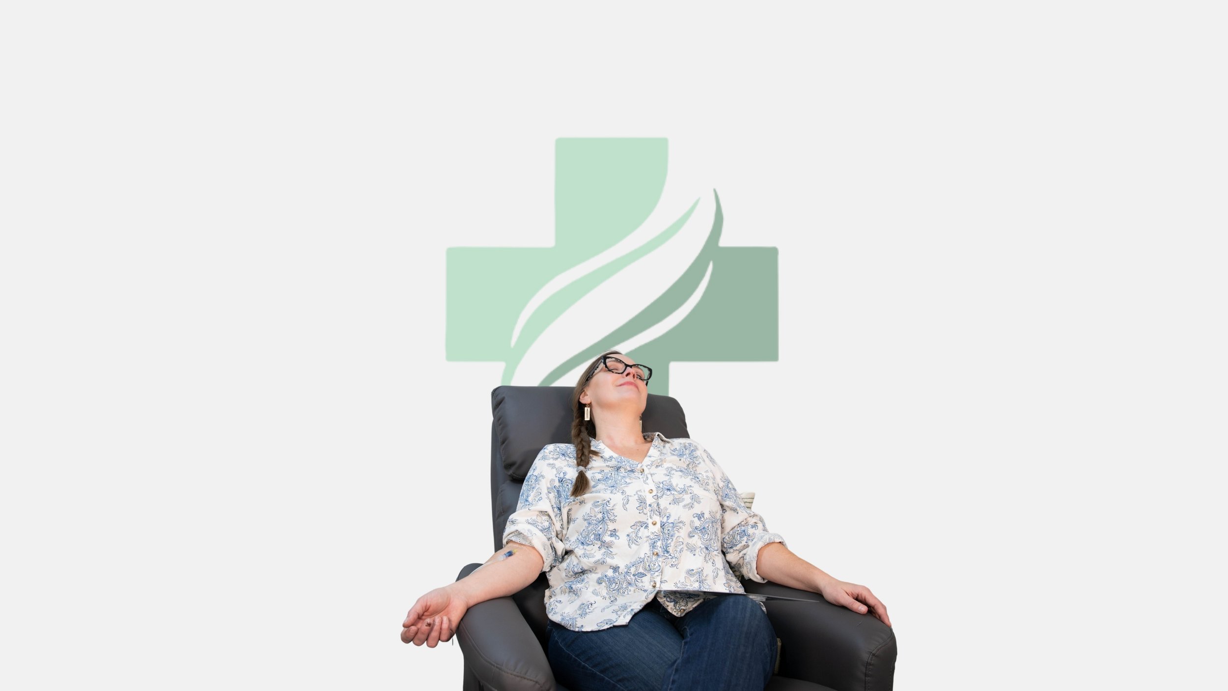 Woman with glasses and braided hair sitting back comfortably in a black chair, eyes closed, smiling, with a medical cross and a stylized leaf logo on the wall behind her.