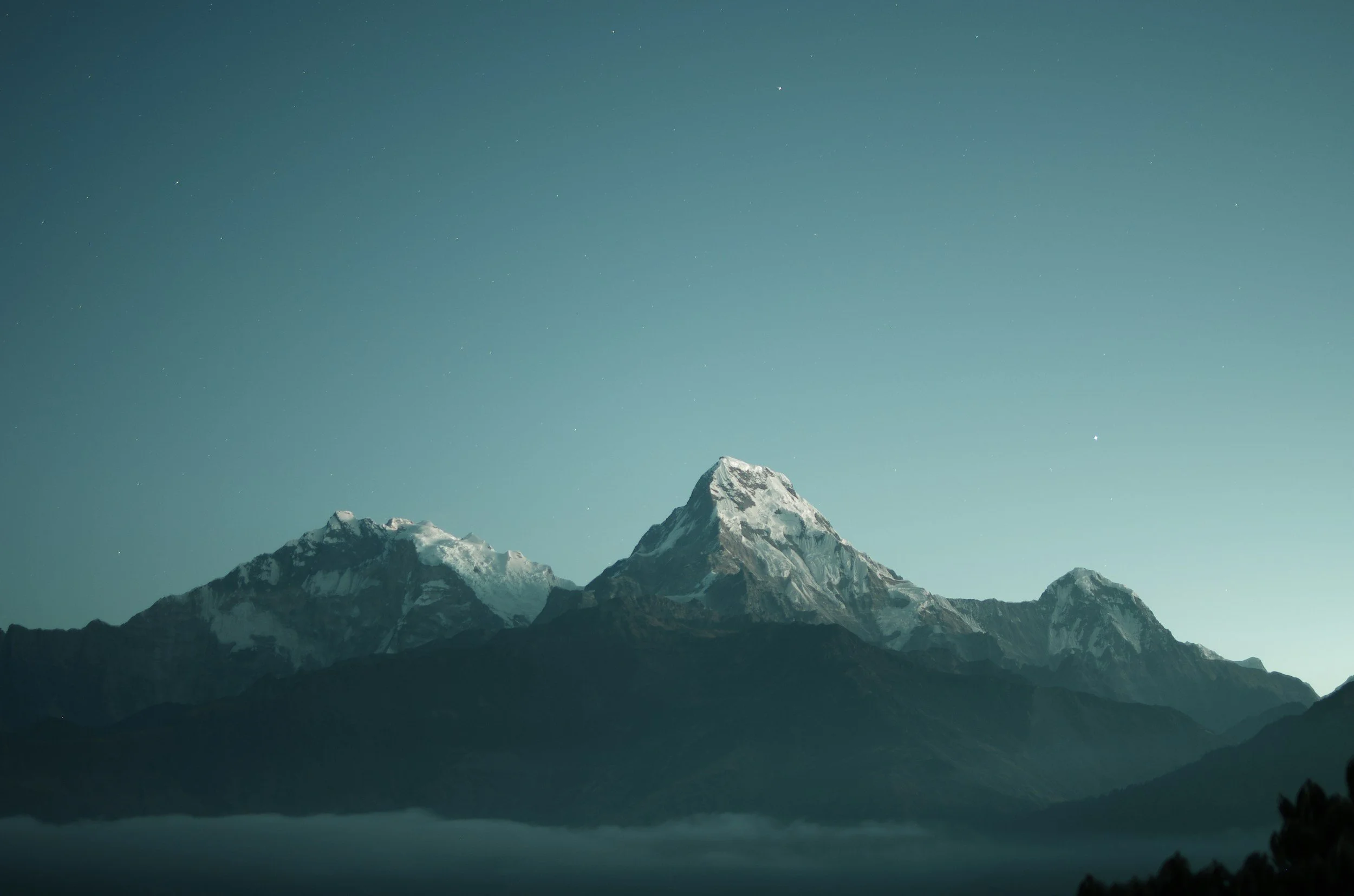 Snow-capped mountains under a clear, starry night sky with some stars visible.