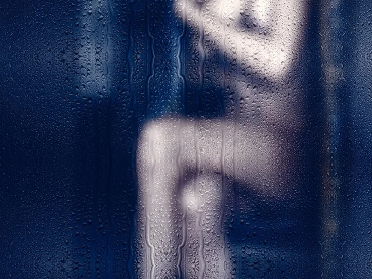 Unscharfe Silhouette einer Person hinter einer nassen Glasscheibe.