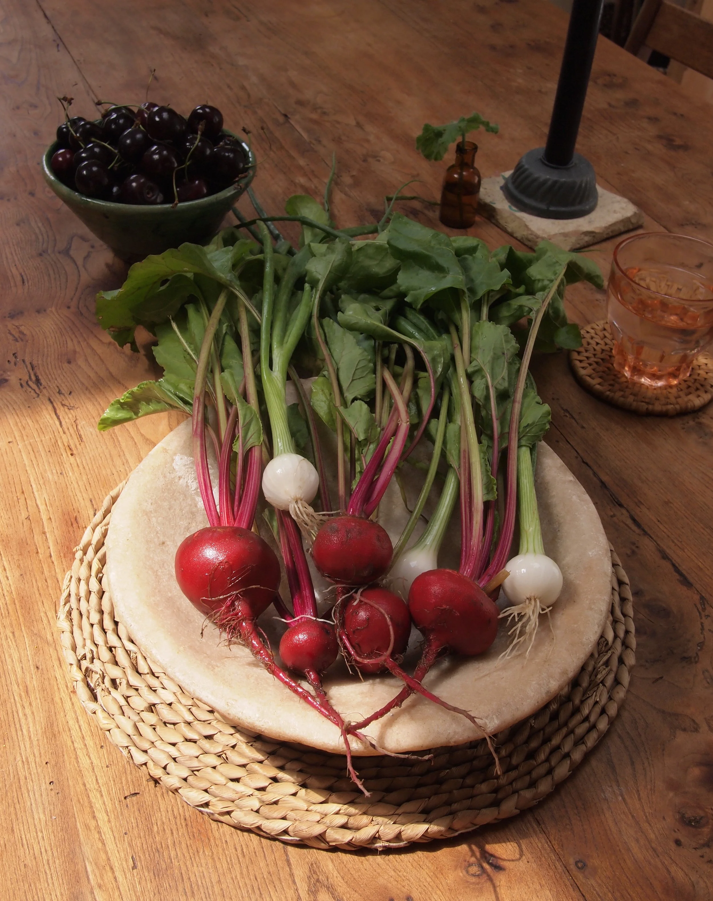 Fresh beets with roots and greens on a stone platter on a wooden table.