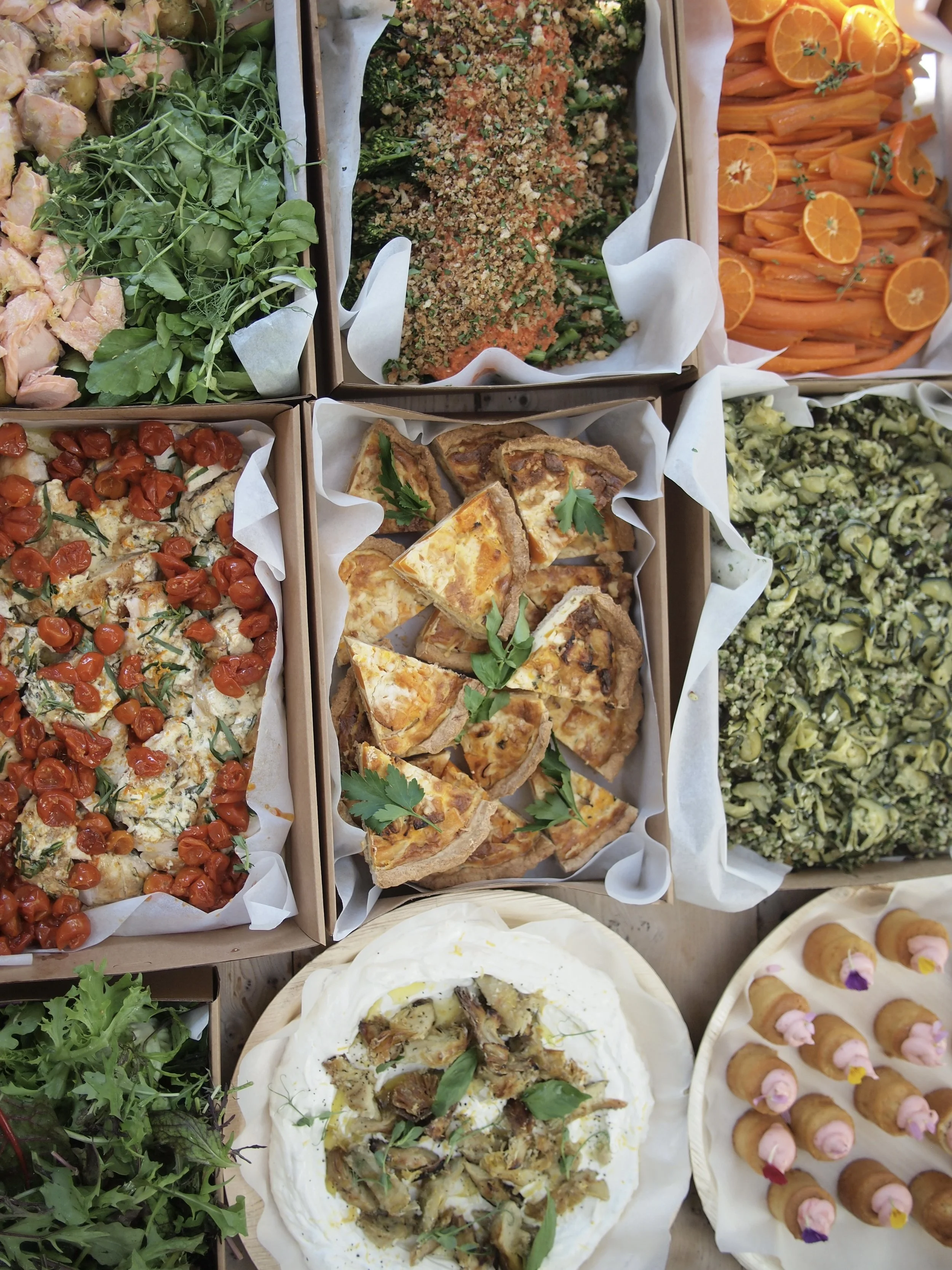 An assortment of dishes including a green salad with greens and chicken, a breaded vegetable casserole, carrots with herbs, cherry tomato and chicken flatbread, quiche slices, a creamy dish with mushrooms and herbs, a green leafy salad, and small pas