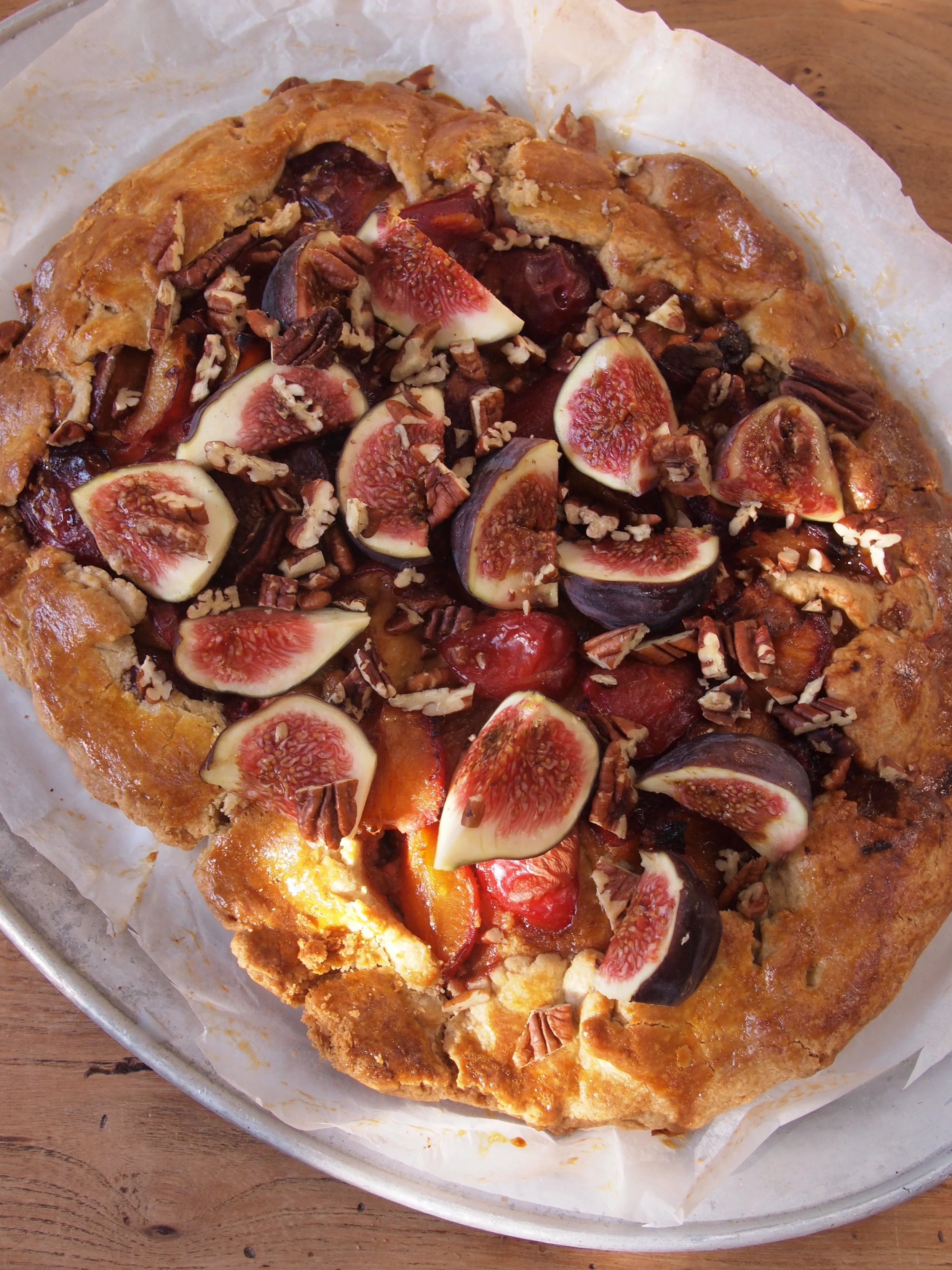 Rustic fruit galette with fresh figs, cherries, and pecans on a parchment-lined baking sheet.