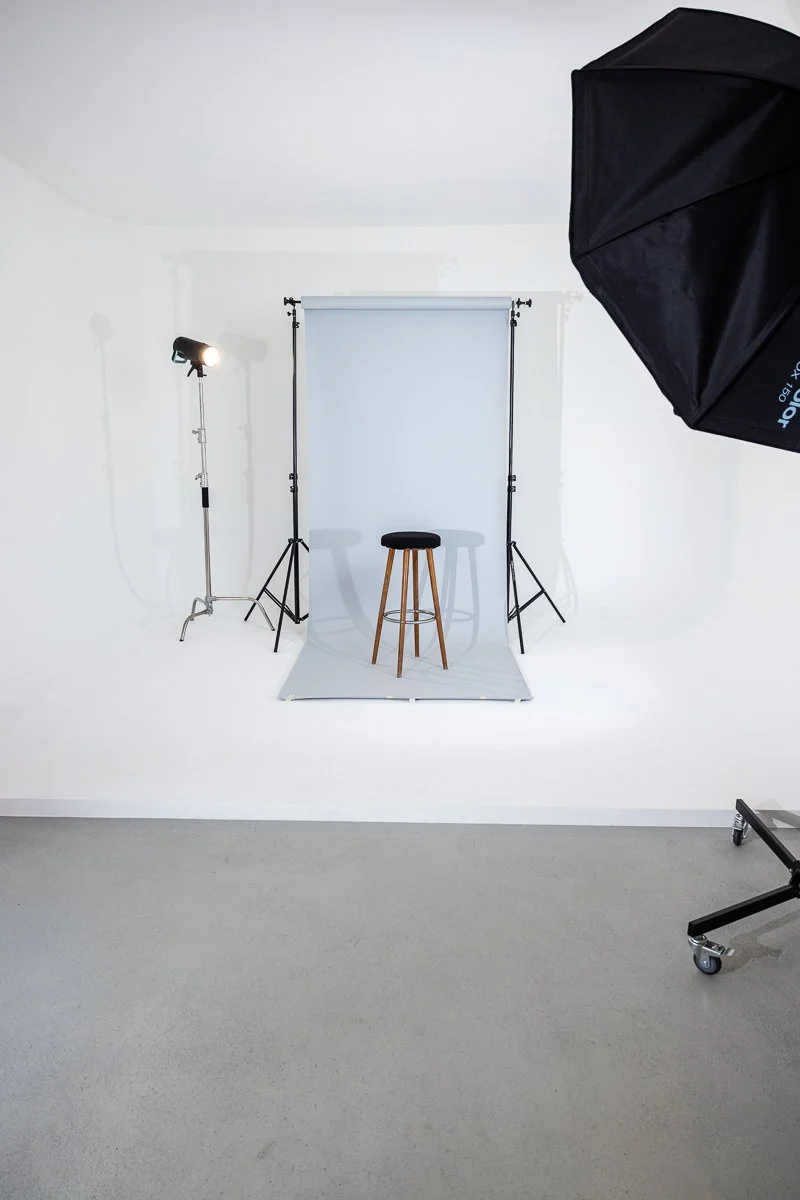 Fotostudio mit grauer Hintergrund, Sessel und professioneller Beleuchtung.