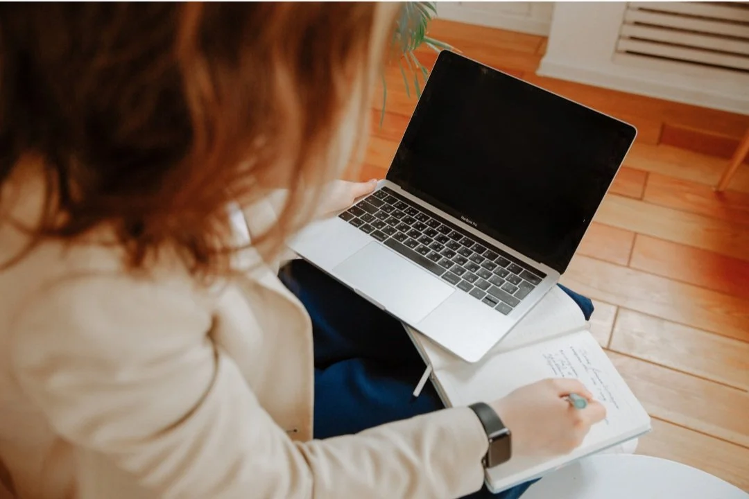 Personne en consultation virtuelle, prenant des notes sur un ordinateur portable