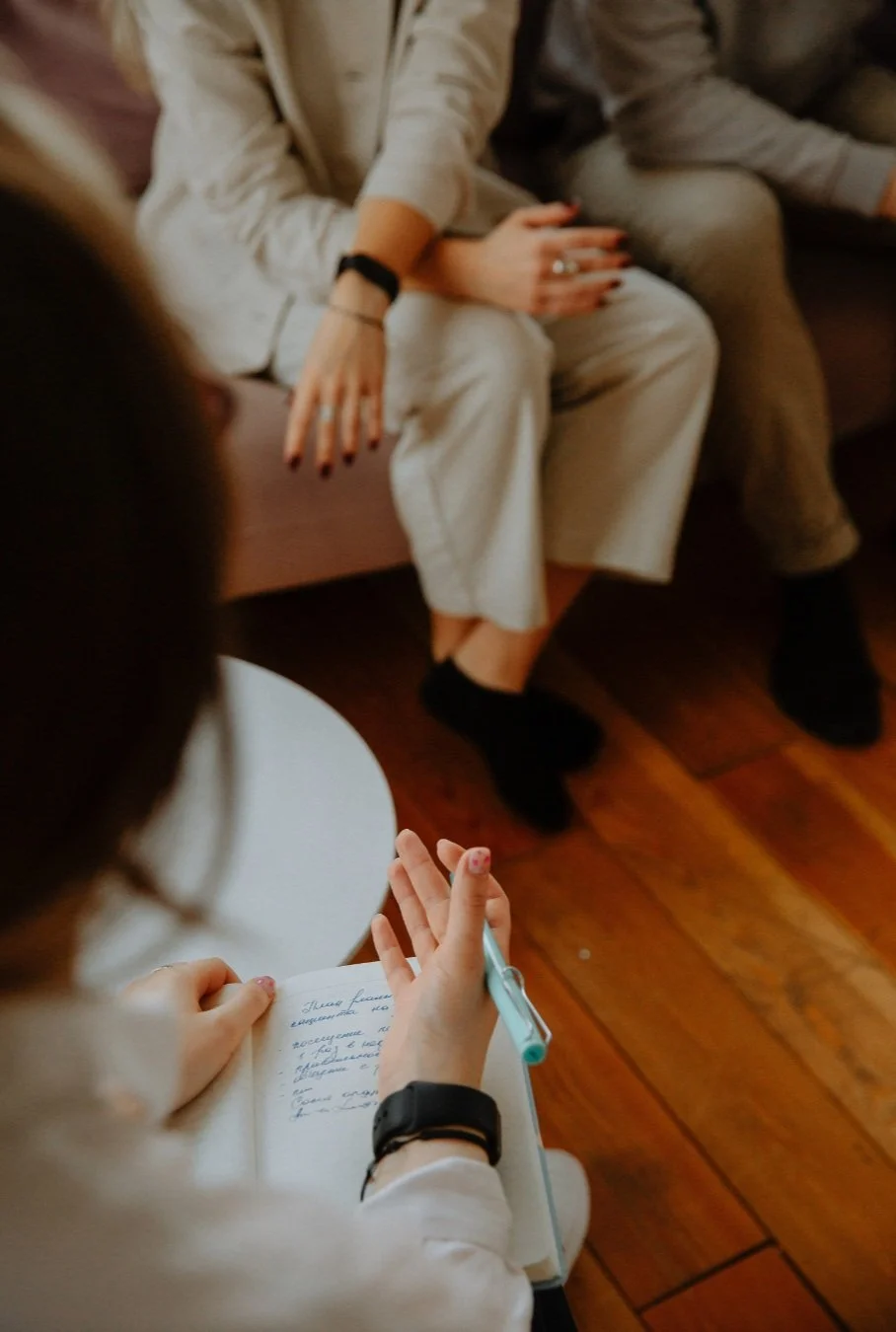 Séance de groupe ou rencontre en thérapie, une personne prend des notes face à deux autres assises sur un canapé.