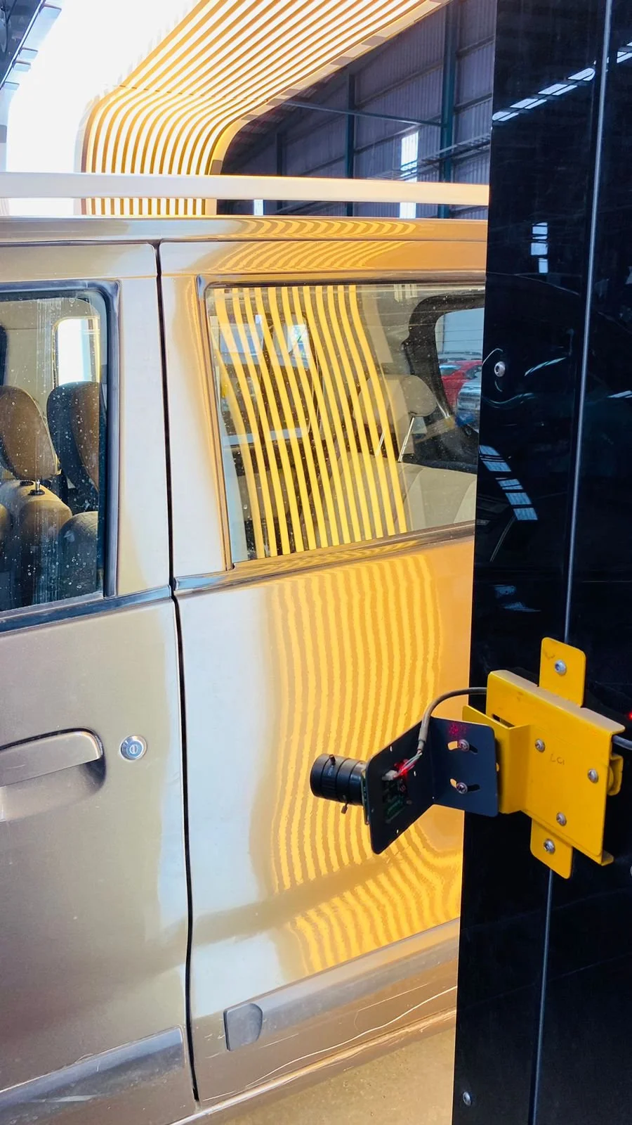 A car with a reflective metal body at an auto show or dealership, and a piece of testing or inspection equipment attached to it.