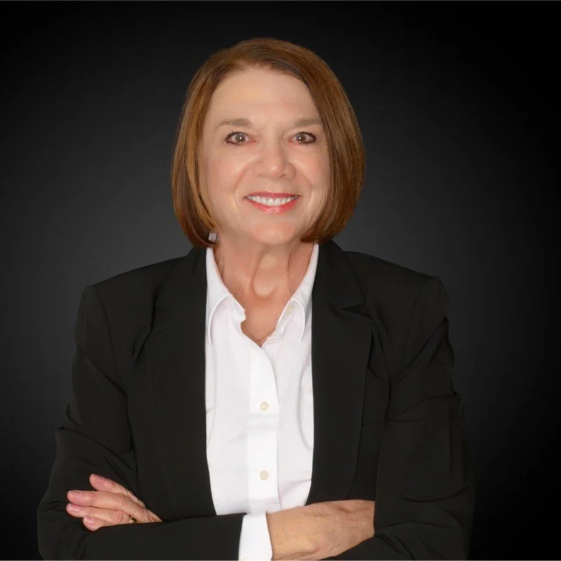 Professional woman smiling in a black suit and white shirt against a dark background.
