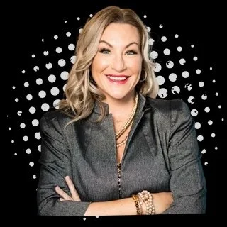 Smiling woman in a gray blazer with a black and white polka dot background.