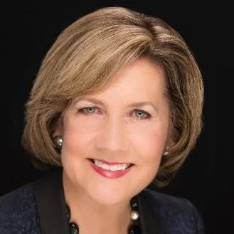 Woman with short blonde hair smiling against a dark background
