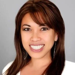 Smiling woman with straight brown hair wearing a white top, posing against a gray background.