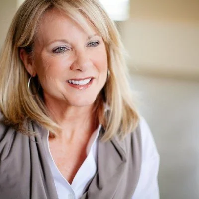 Smiling woman with blonde hair wearing a scarf and white blouse
