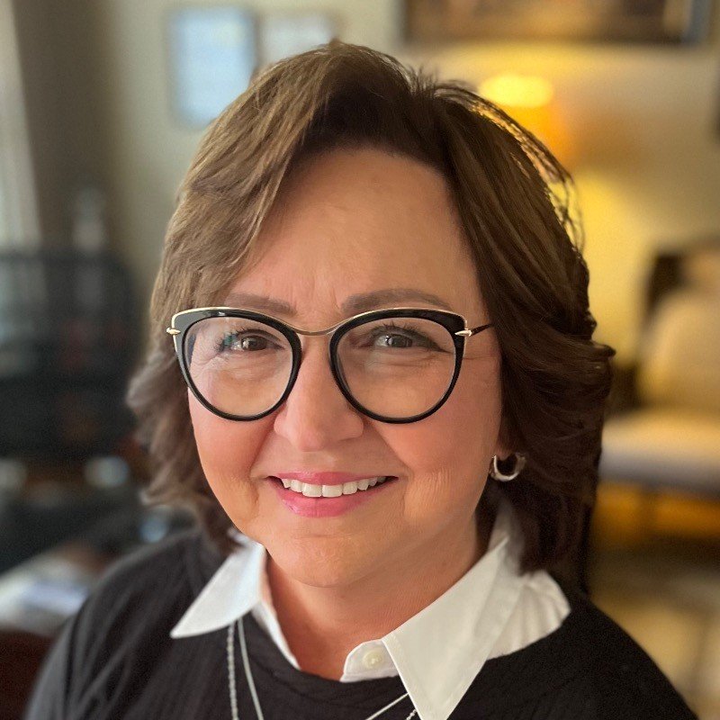 Person wearing glasses and smiling indoors, with a blurred background.