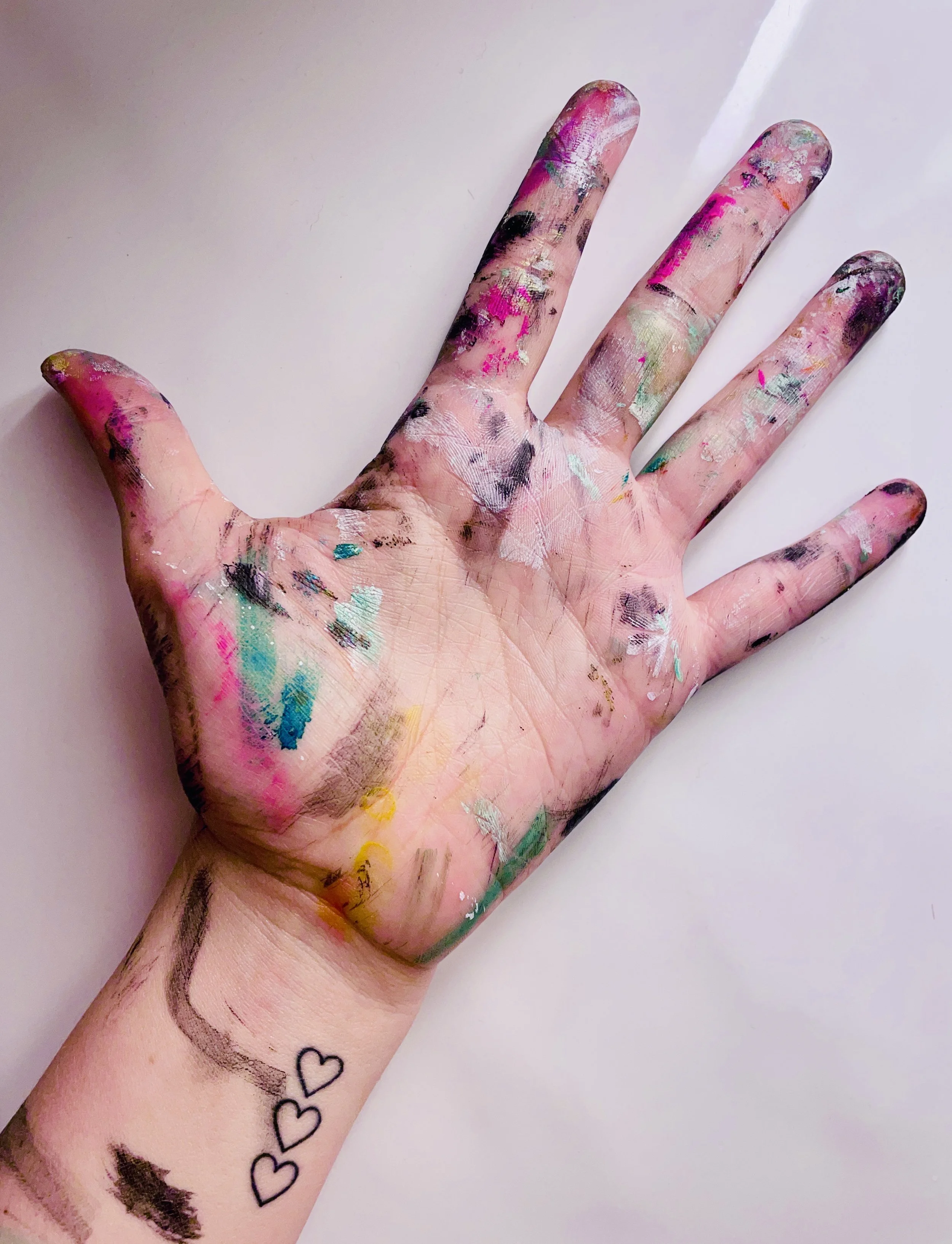 Hånd dekket av maling i ulike farger, mot en lys bakgrunn.