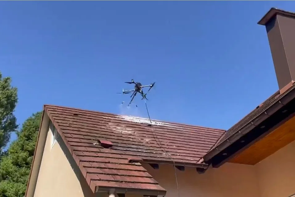 Un drone équipé de bras et de plusieurs hélices est en train de pulvériser un produit sur le toit d'une maison.