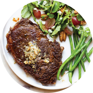 Plate with steak topped with pecan compound butter and salad topped with pecans