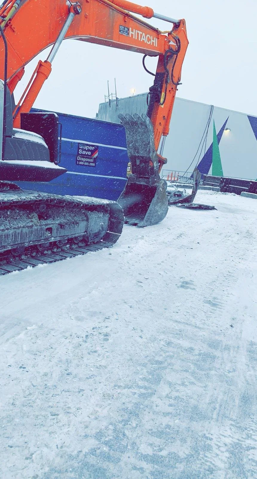 Orange Hitachi excavator on a snowy construction site next to a blue container.