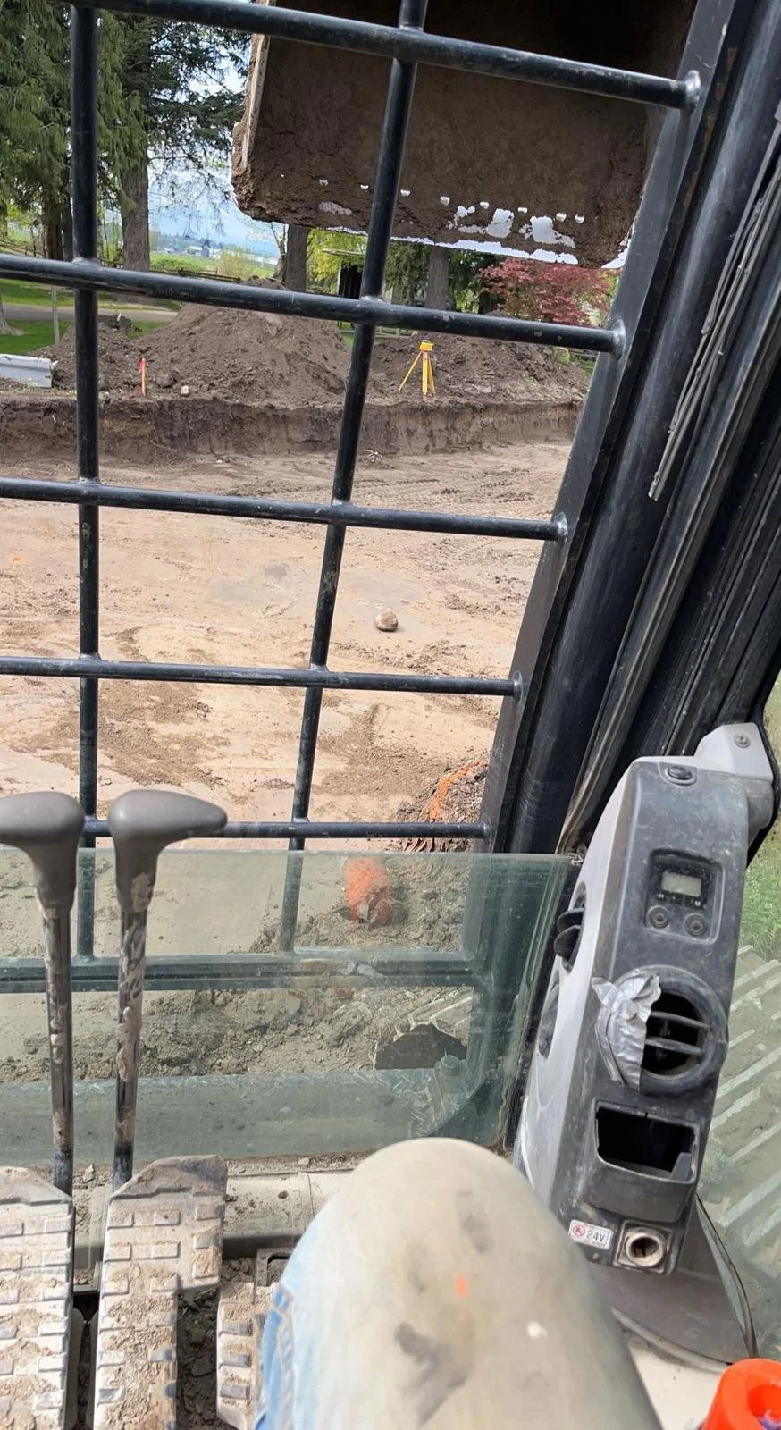 View from inside a construction vehicle cabin with dirt and excavation site outside.