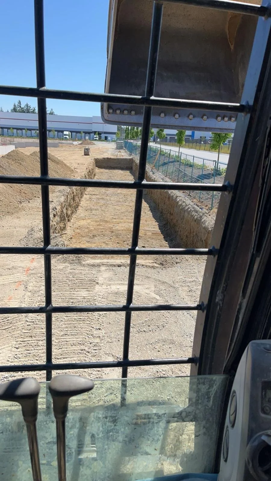 View from inside an excavator overlooking a construction site with trenches and dirt piles.