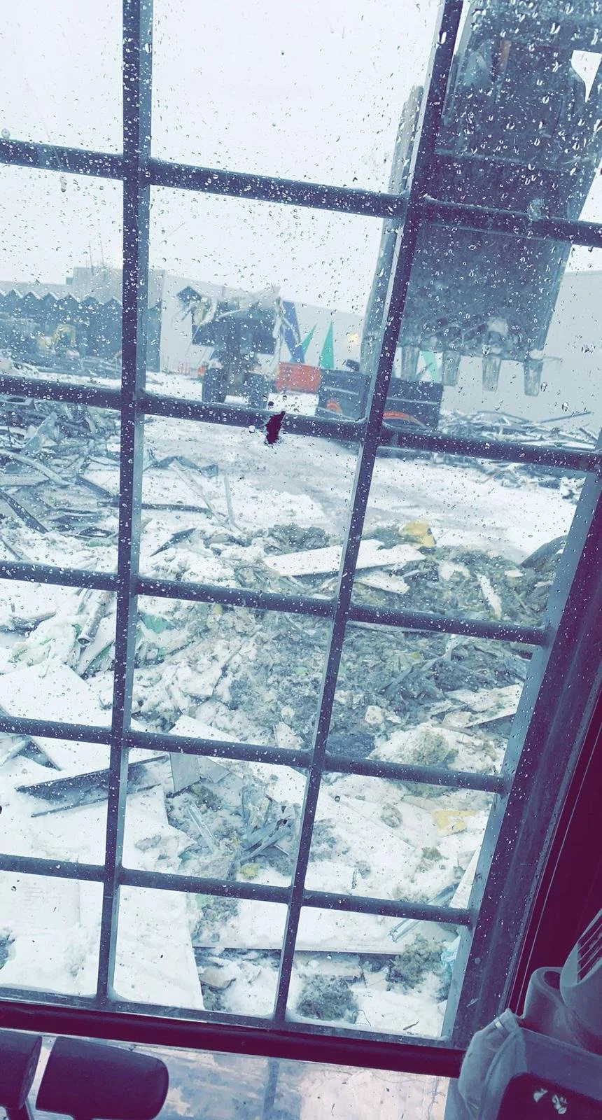 View through a rainy window showing snow-covered debris and a construction site with machinery.