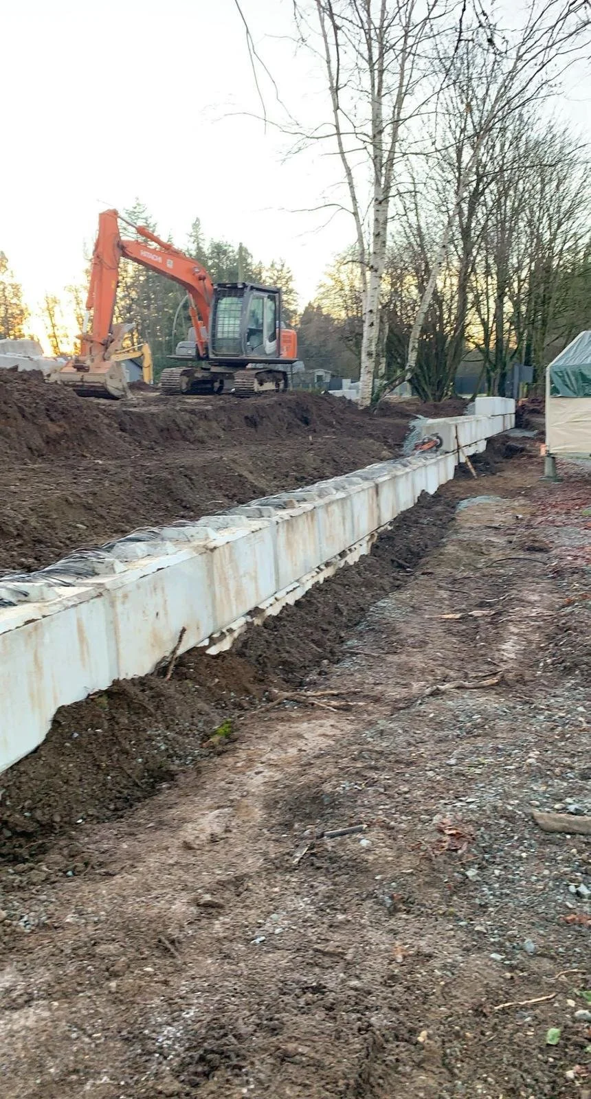 Excavator at construction site with trenches and concrete structures