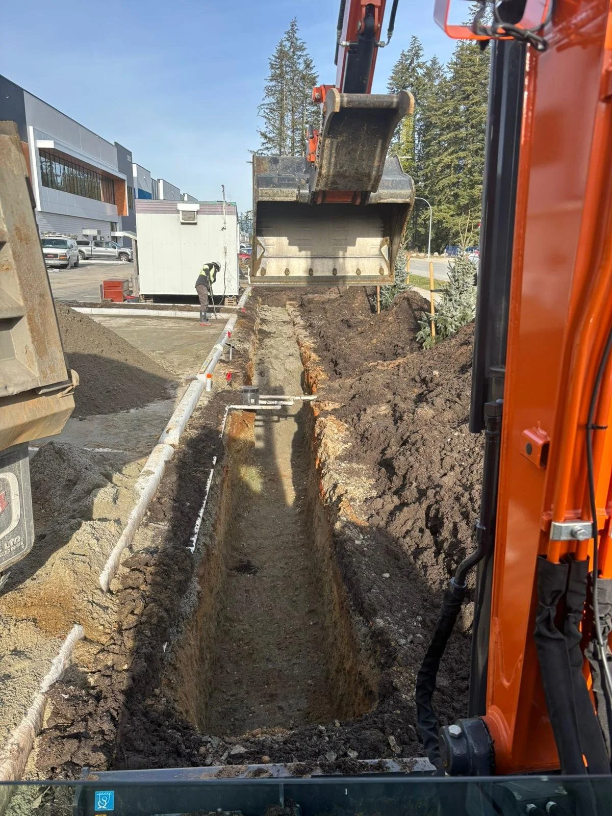 Excavator digging a trench at a construction site with worker nearby.