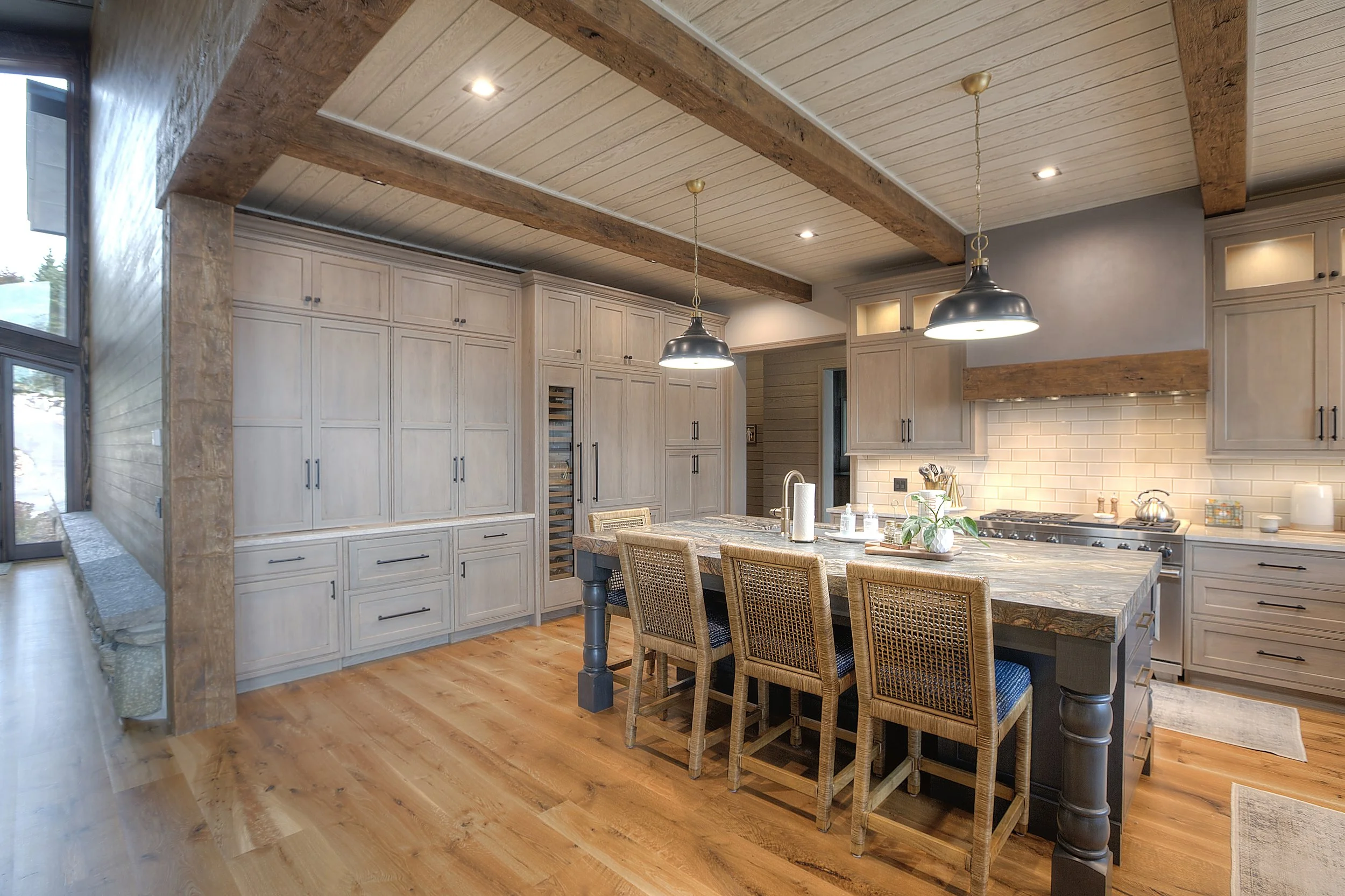 Modern rustic kitchen with wooden cabinetry, an island with wicker chairs, pendant lights, and hardwood floors.