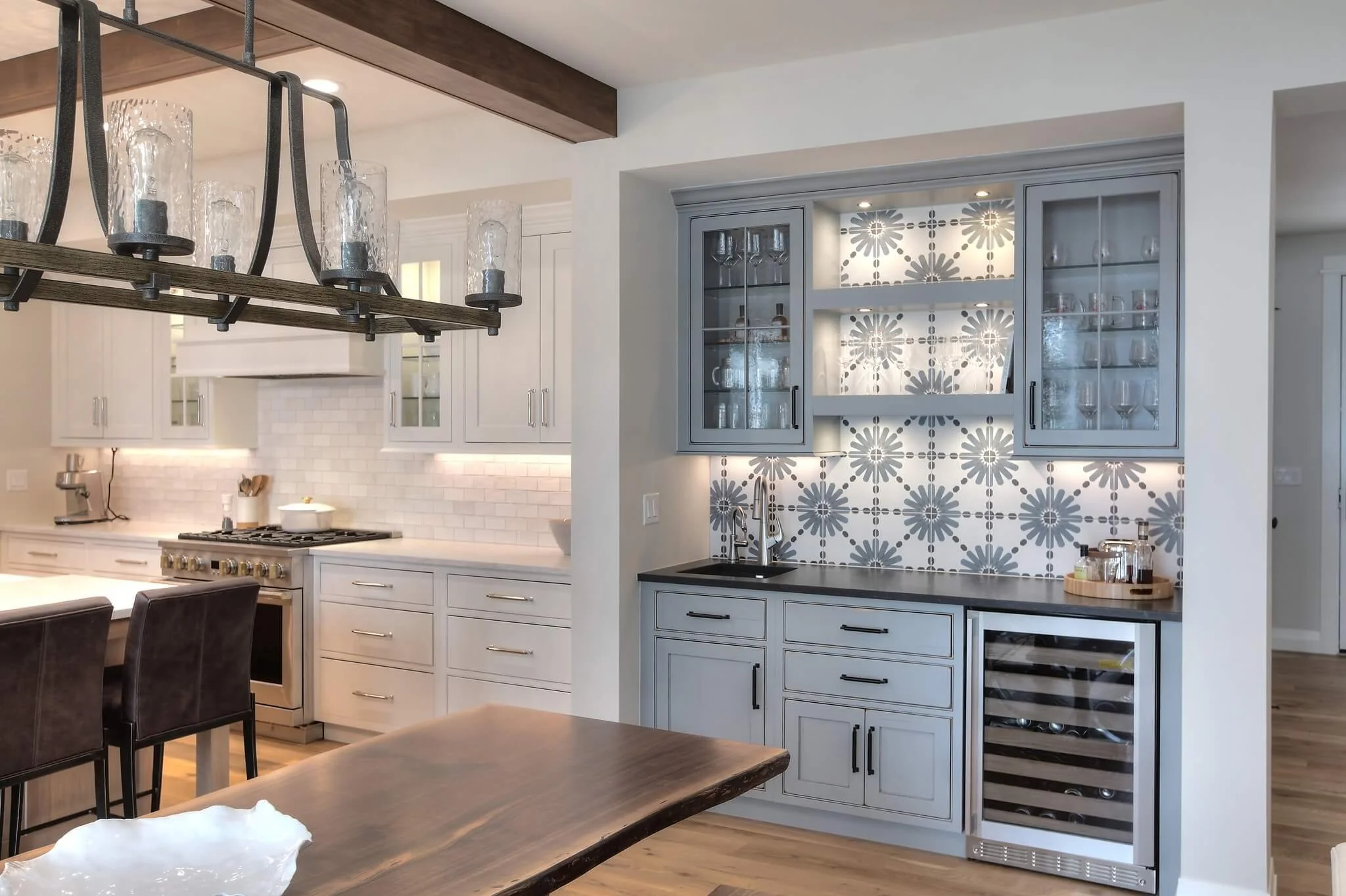 Modern kitchen with white and gray cabinets, decorative tile backsplash, wine cooler, and industrial-style lighting.