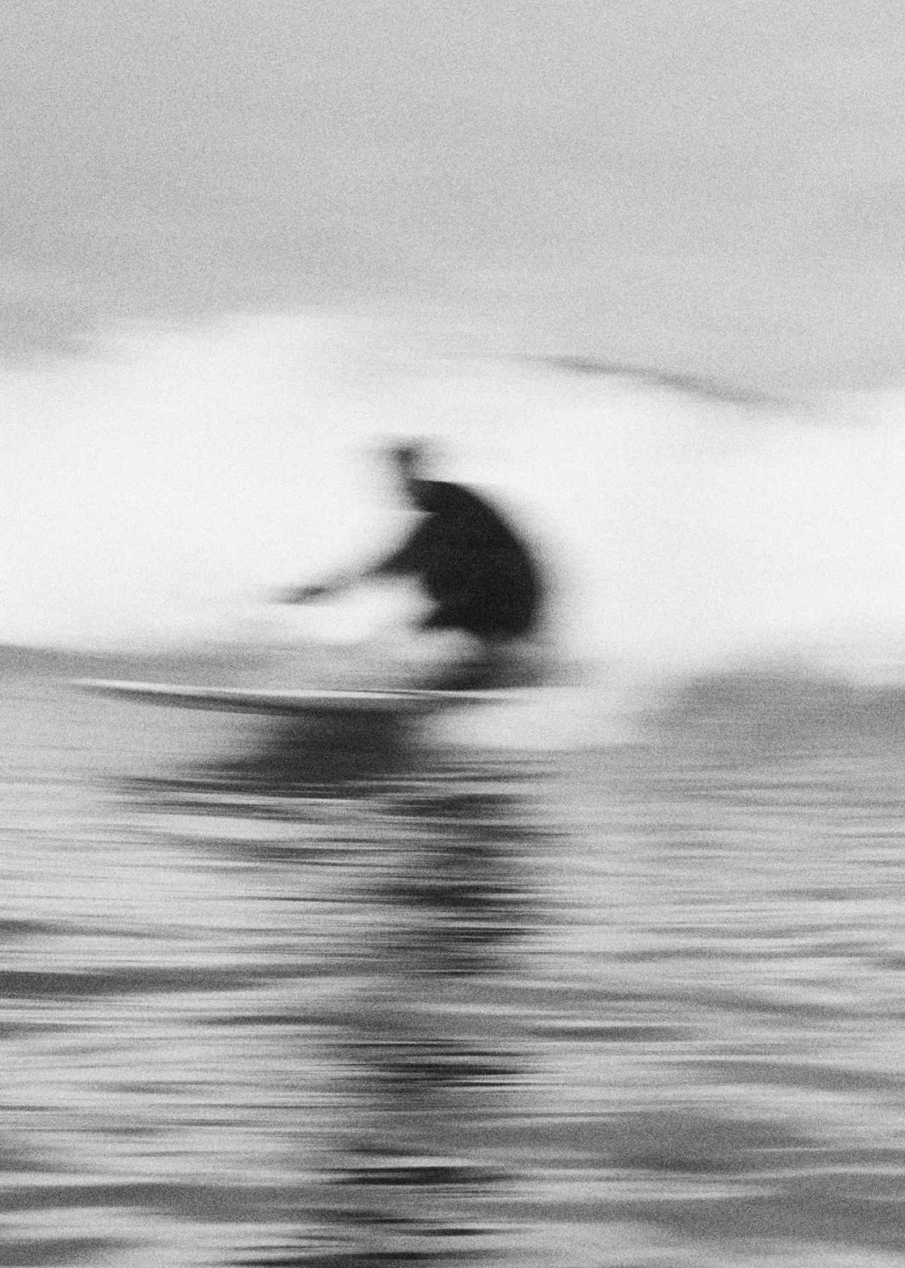 A black and white photo of a person surfing, with the motion blur effect creating a sense of movement on the water.
