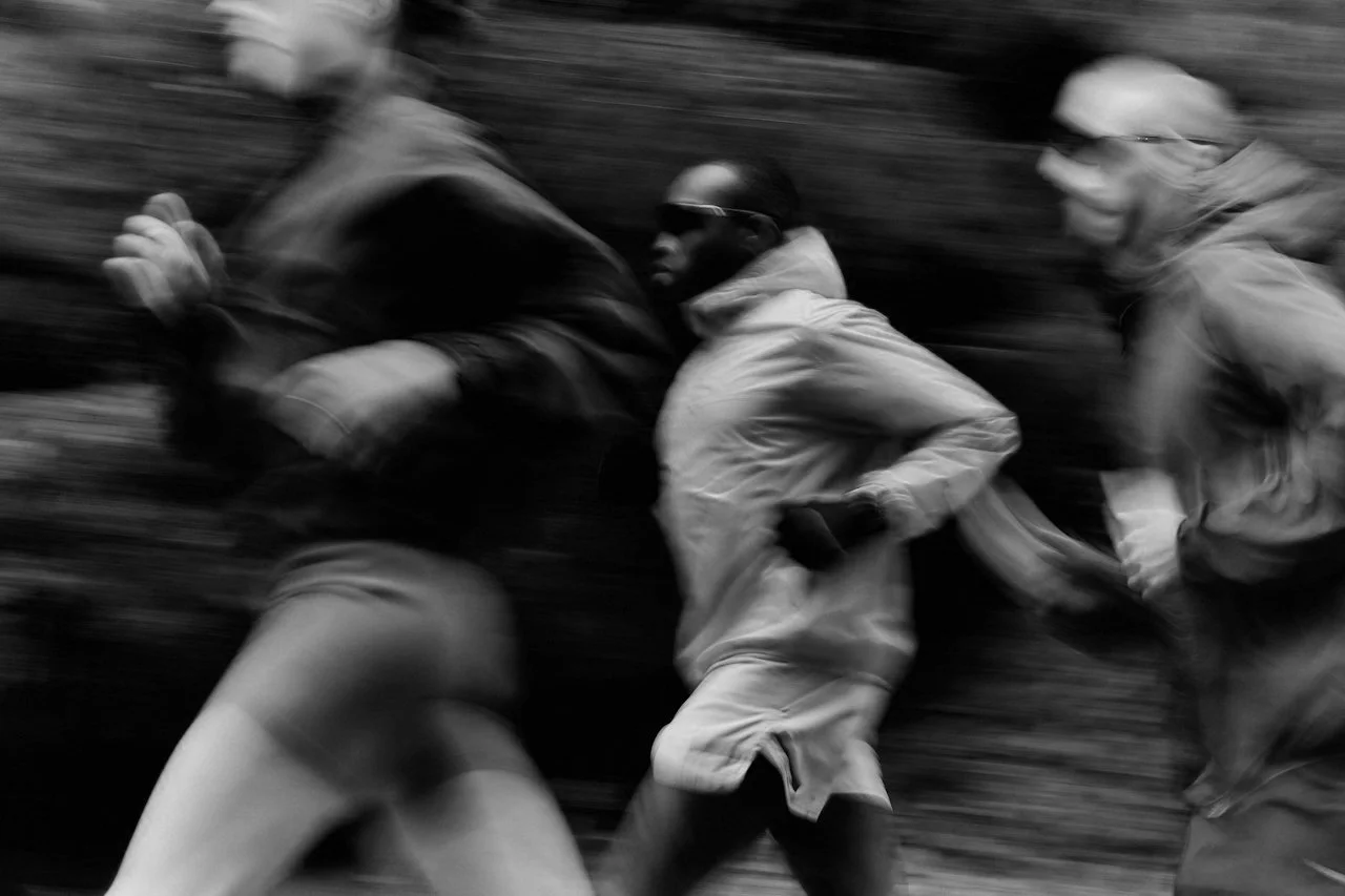 Black and white photo of three runners in motion, blurred background, wearing athletic clothing